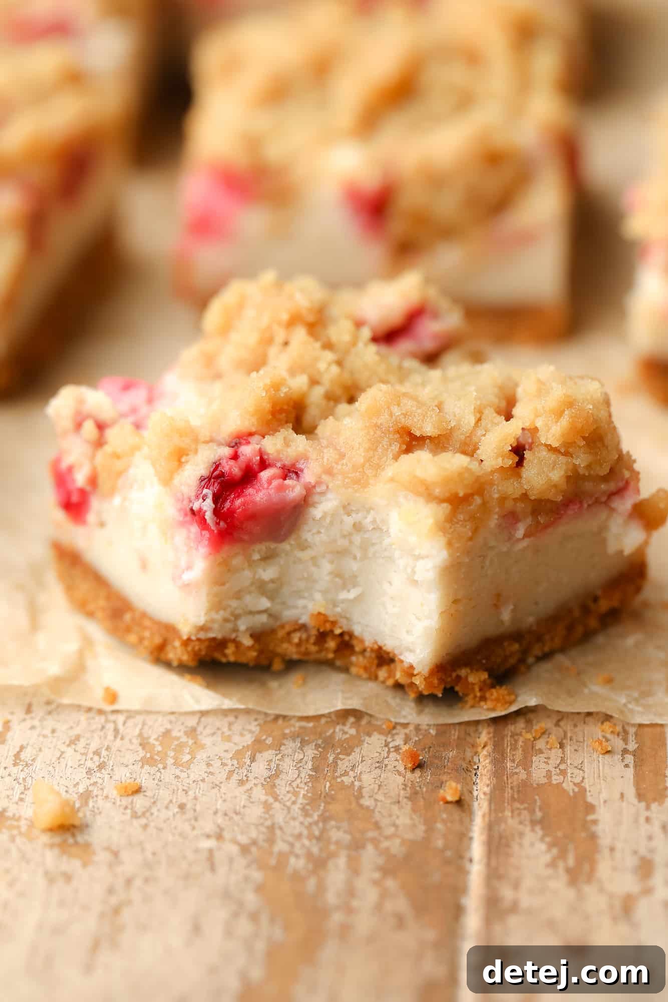 A single Vegan Strawberry Cheesecake Crumble Bar with a bite removed, revealing the layers of crust, creamy cheesecake, strawberries, and crumble.