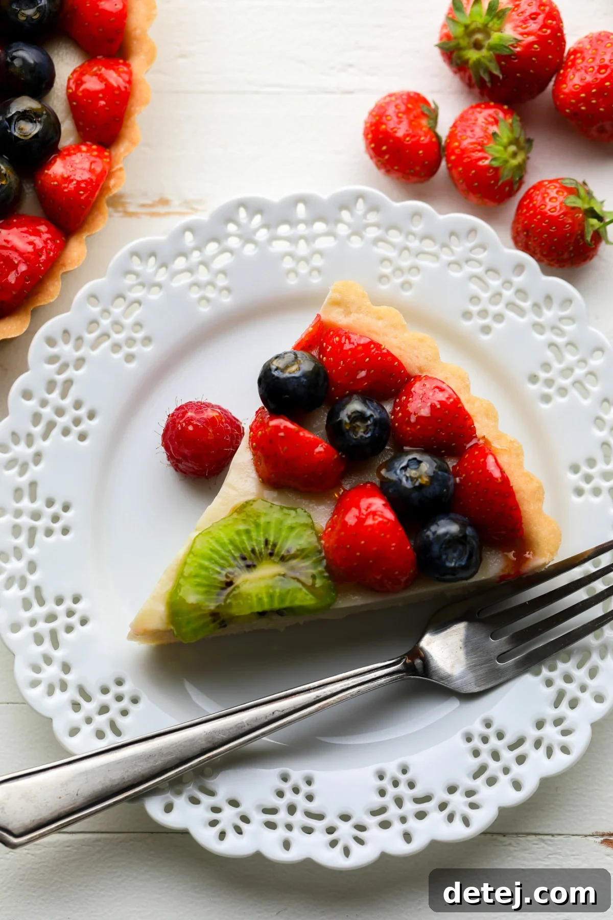 A perfectly portioned slice of vegan fruit tart on a white plate, showcasing its beautiful layers of crust, custard, and fresh fruit.