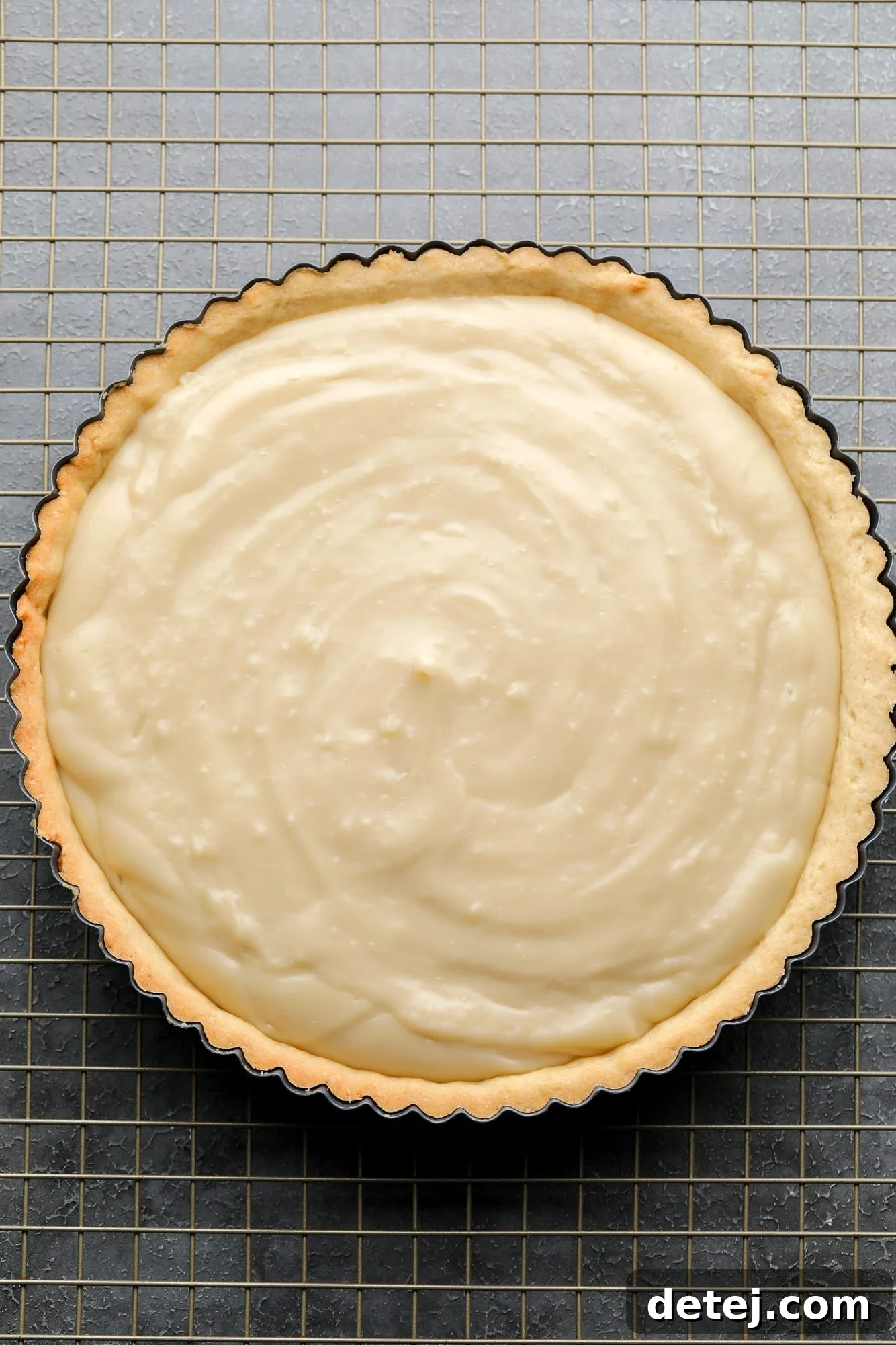 Creamy vegan custard setting inside a baked vegan tart crust, resting on a wire rack.