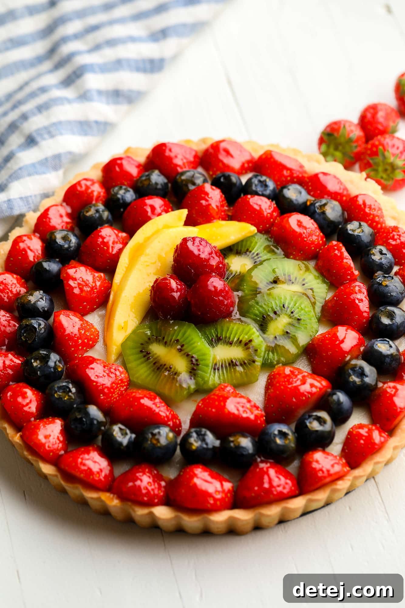 A close-up shot of a magnificent vegan fruit tart, gleaming with glazed berries, kiwi, and mango, showcasing its irresistible freshness.