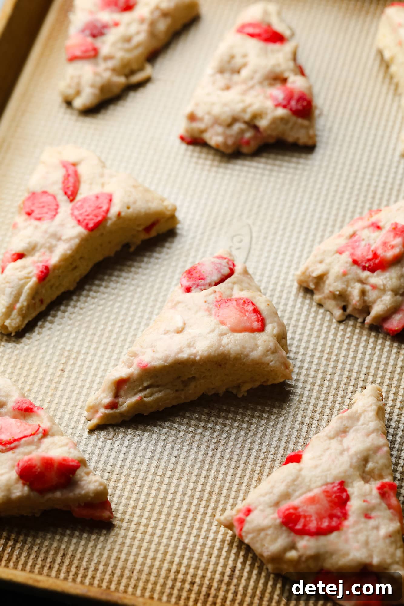 Unbaked vegan strawberry scone dough pieces arranged on a baking sheet, ready for the oven.