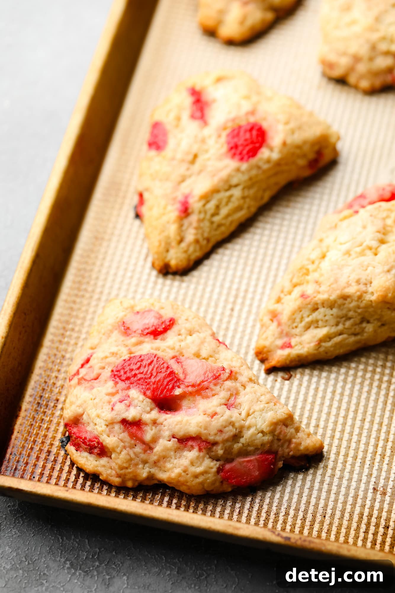 Freshly baked vegan strawberry scones resting on a baking sheet, golden brown and ready for glazing.