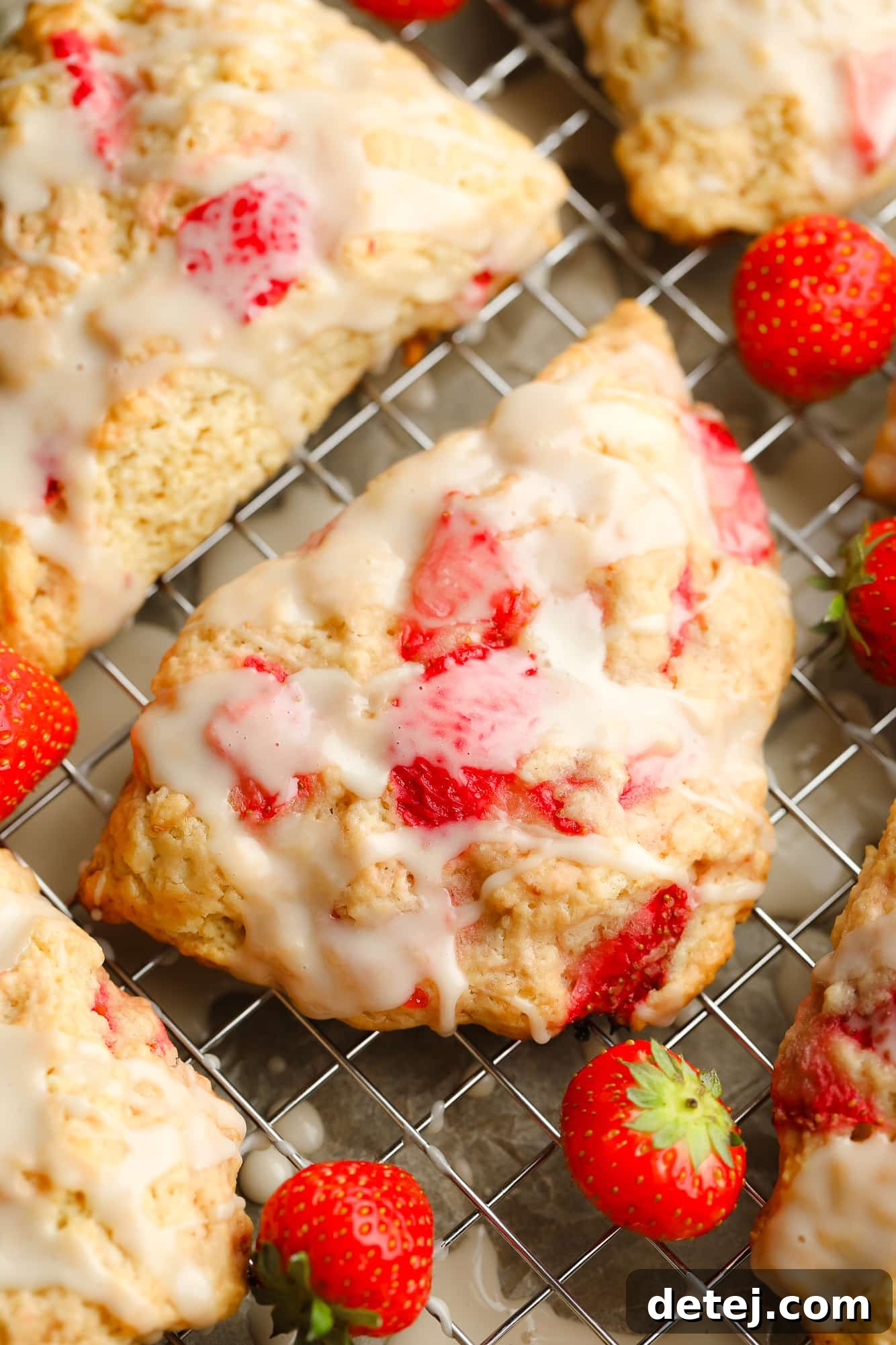 A delectable close-up of a single baked strawberry scone, generously topped with vanilla glaze and showing bits of fresh strawberry.