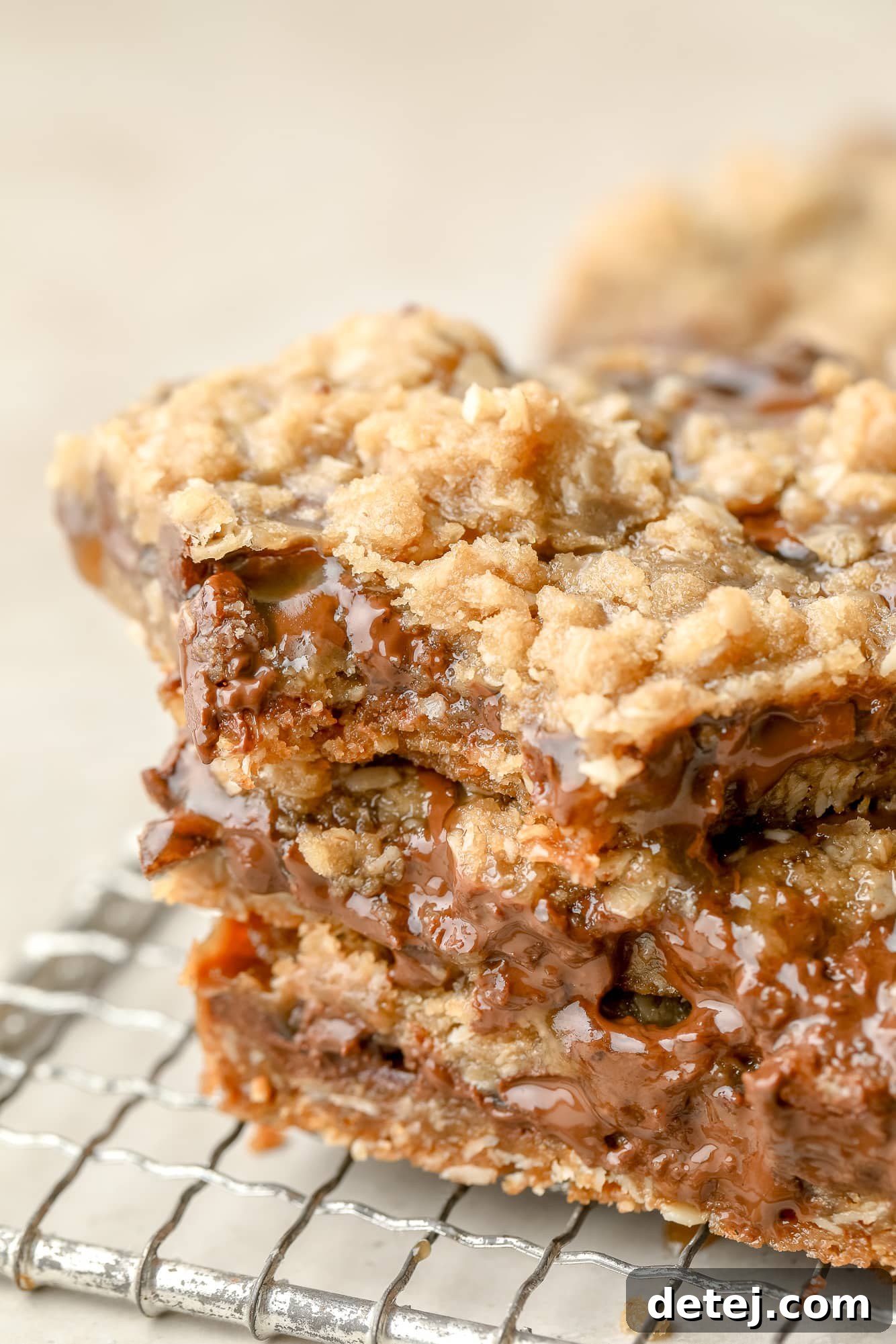 A close-up shot of a stack of three Vegan Carmelitas, with one bar having a bite taken out, clearly revealing the soft, gooey caramel and melted chocolate layers nestled within the chewy oat crust.