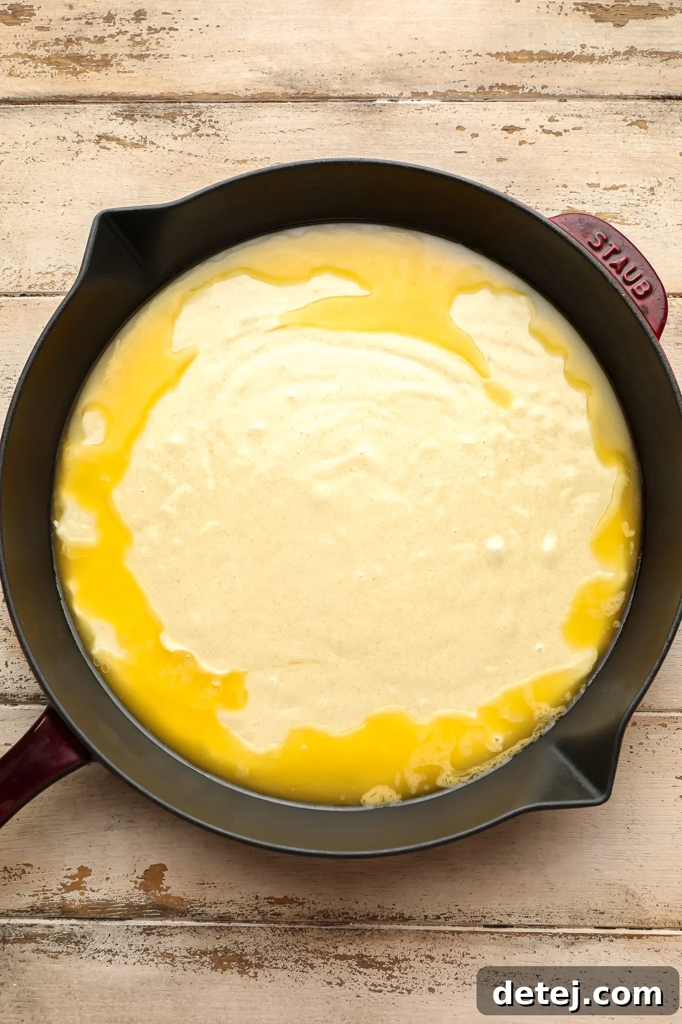 Melted vegan butter topped with the smooth, pale cobbler dough in a black cast iron skillet, before adding berries.