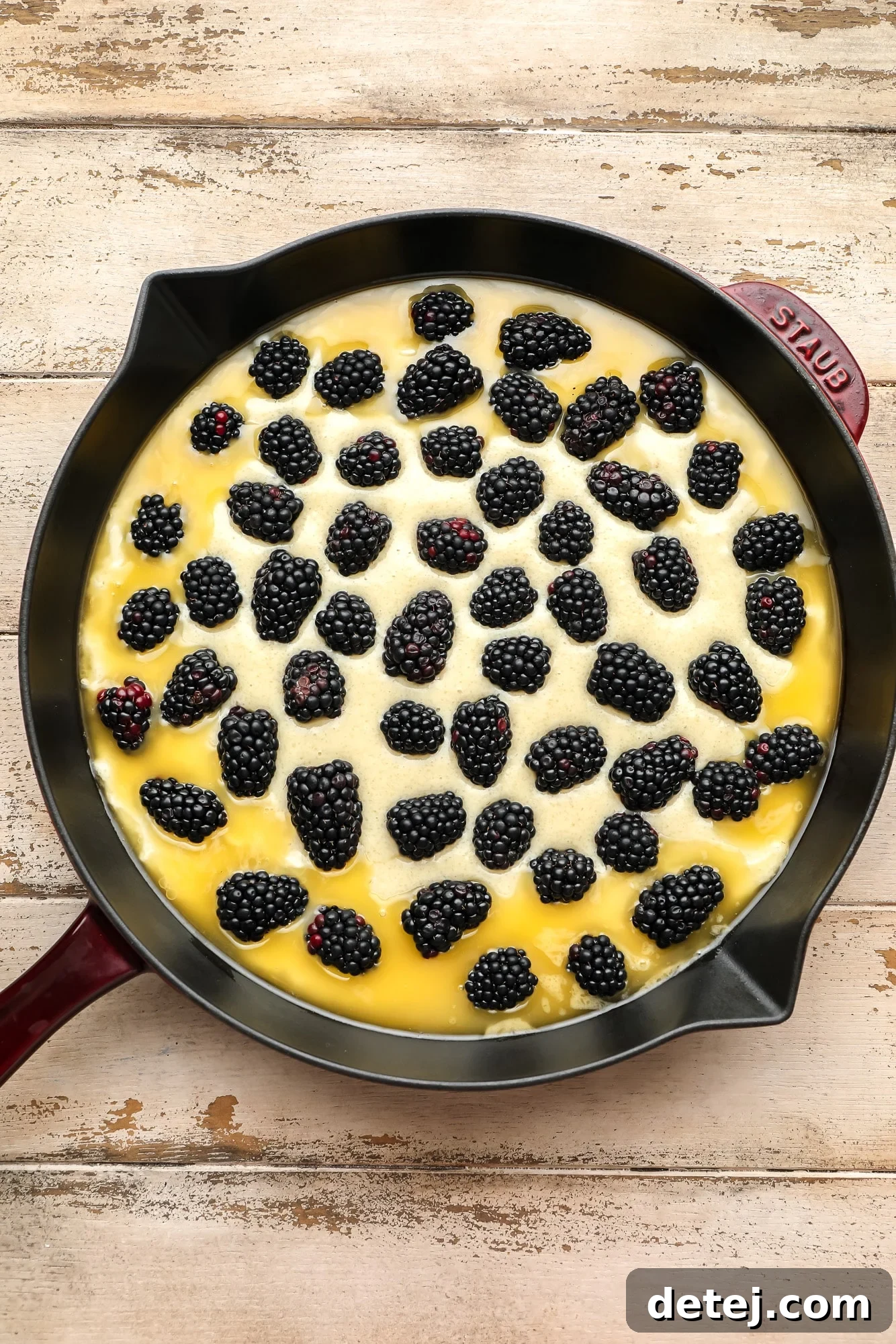 An unbaked and assembled blackberry cobbler, with blackberries scattered over the dough, sitting in a black skillet, ready for the oven.