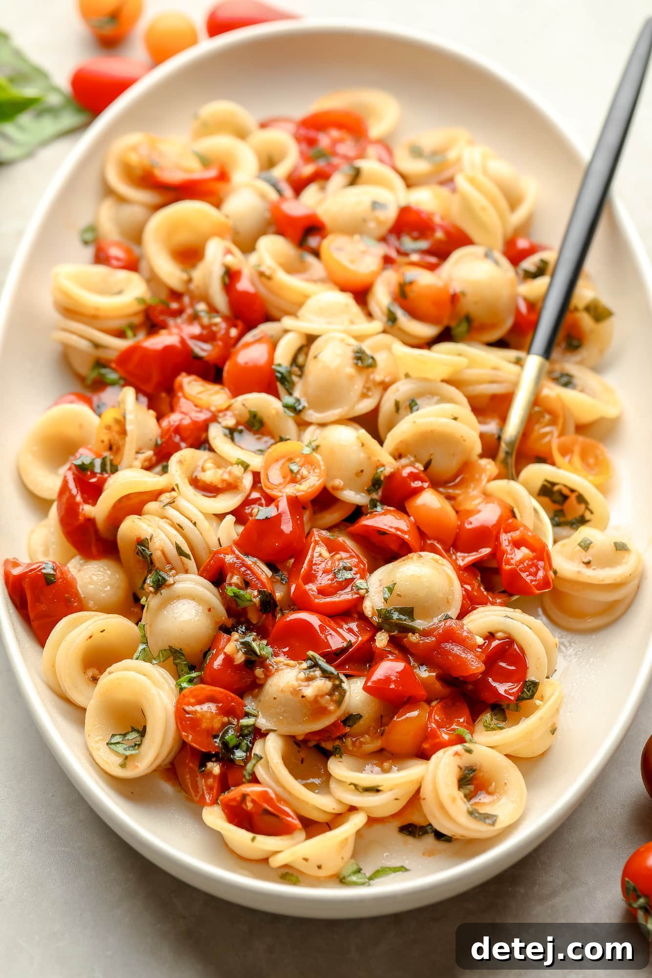 Roasted Tomato Pasta in a white serving dish with a spoon, generously garnished with fresh basil leaves and vegan parmesan cheese.