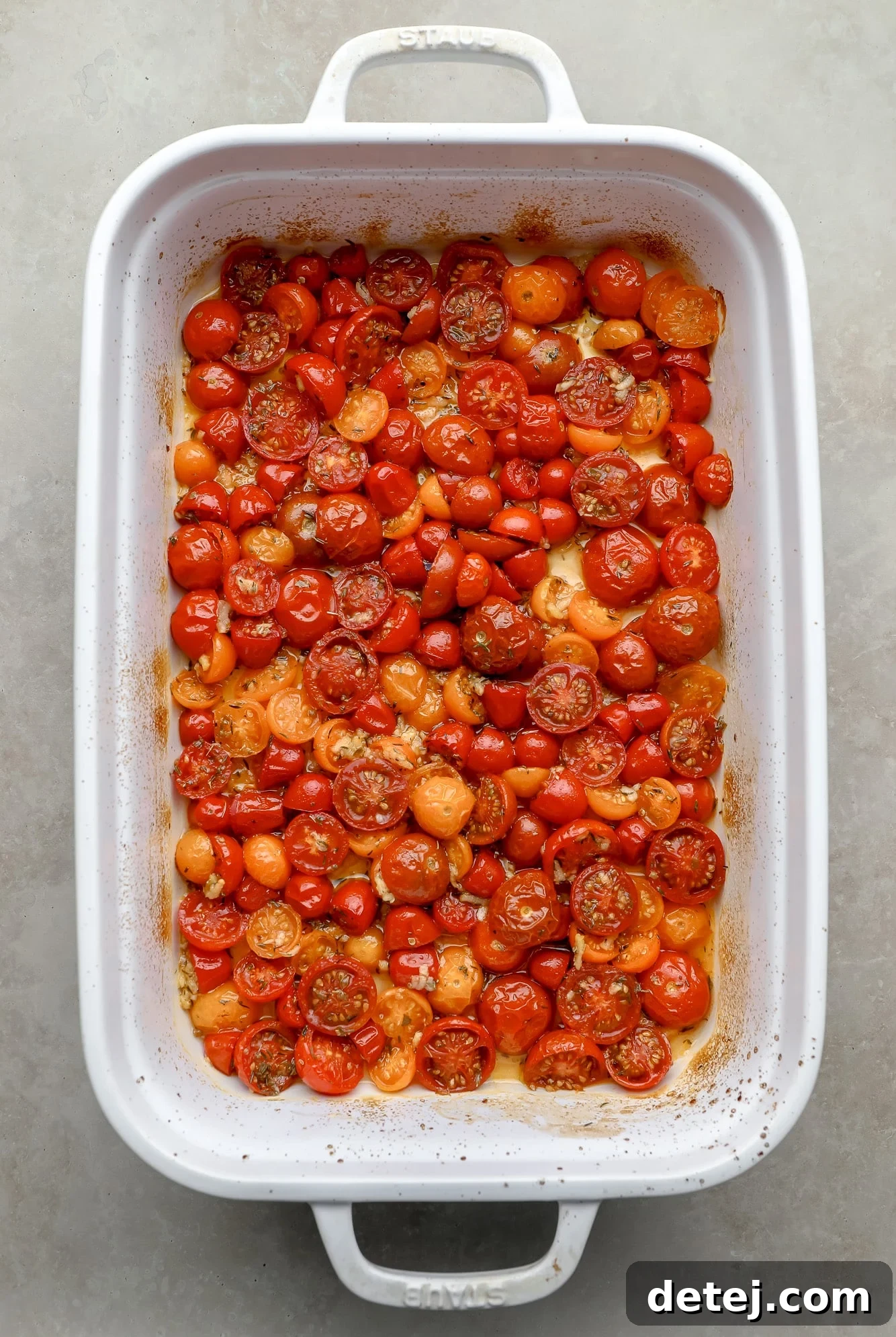 Perfectly roasted cherry tomatoes in a large white baking dish, showing a glistening, blistered appearance and rich red color after cooking.