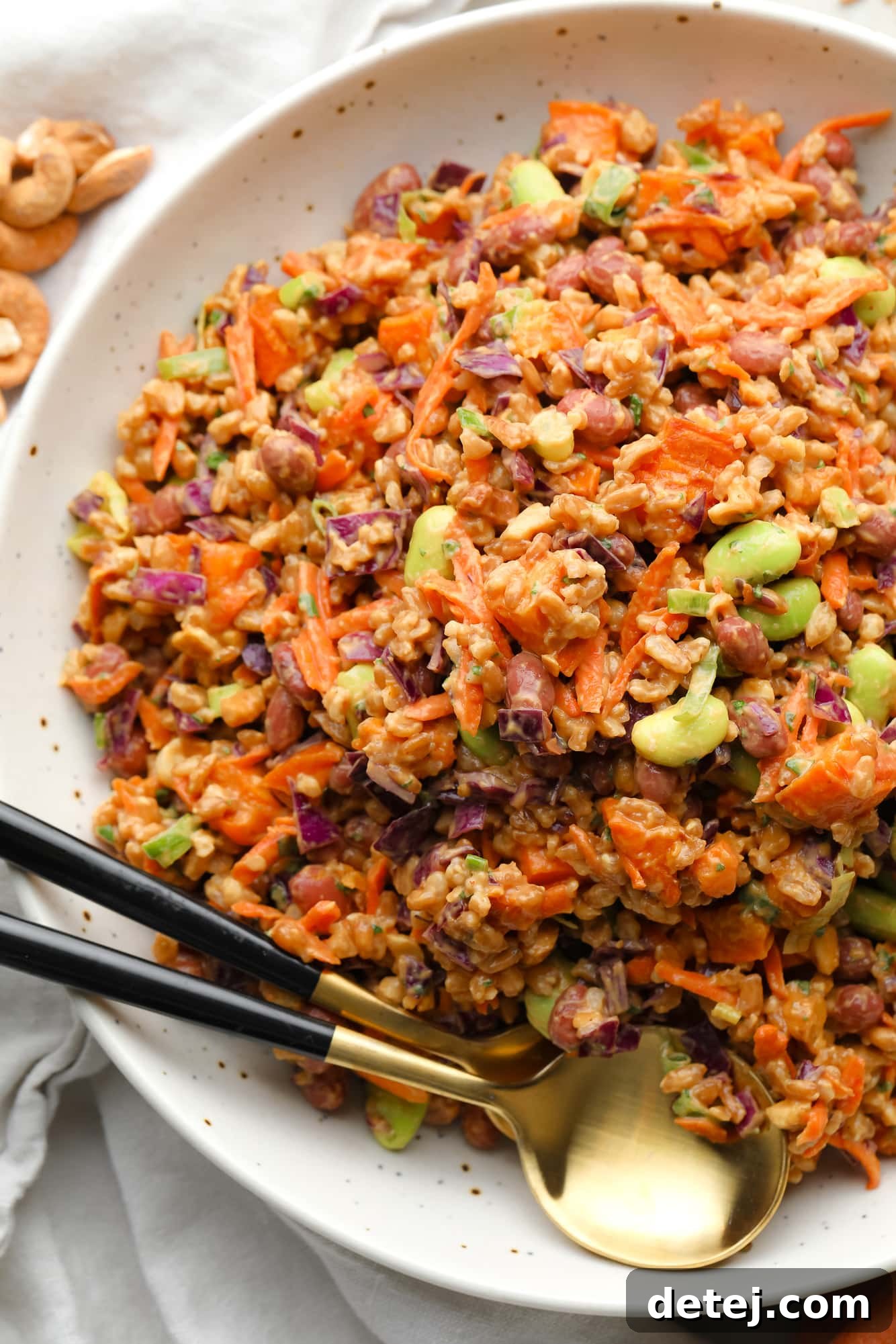 Spicy Peanut Farro Power Bowl 2 farro salad dressed in peanut sauce in a large white bowl with a gold spoon on the side.