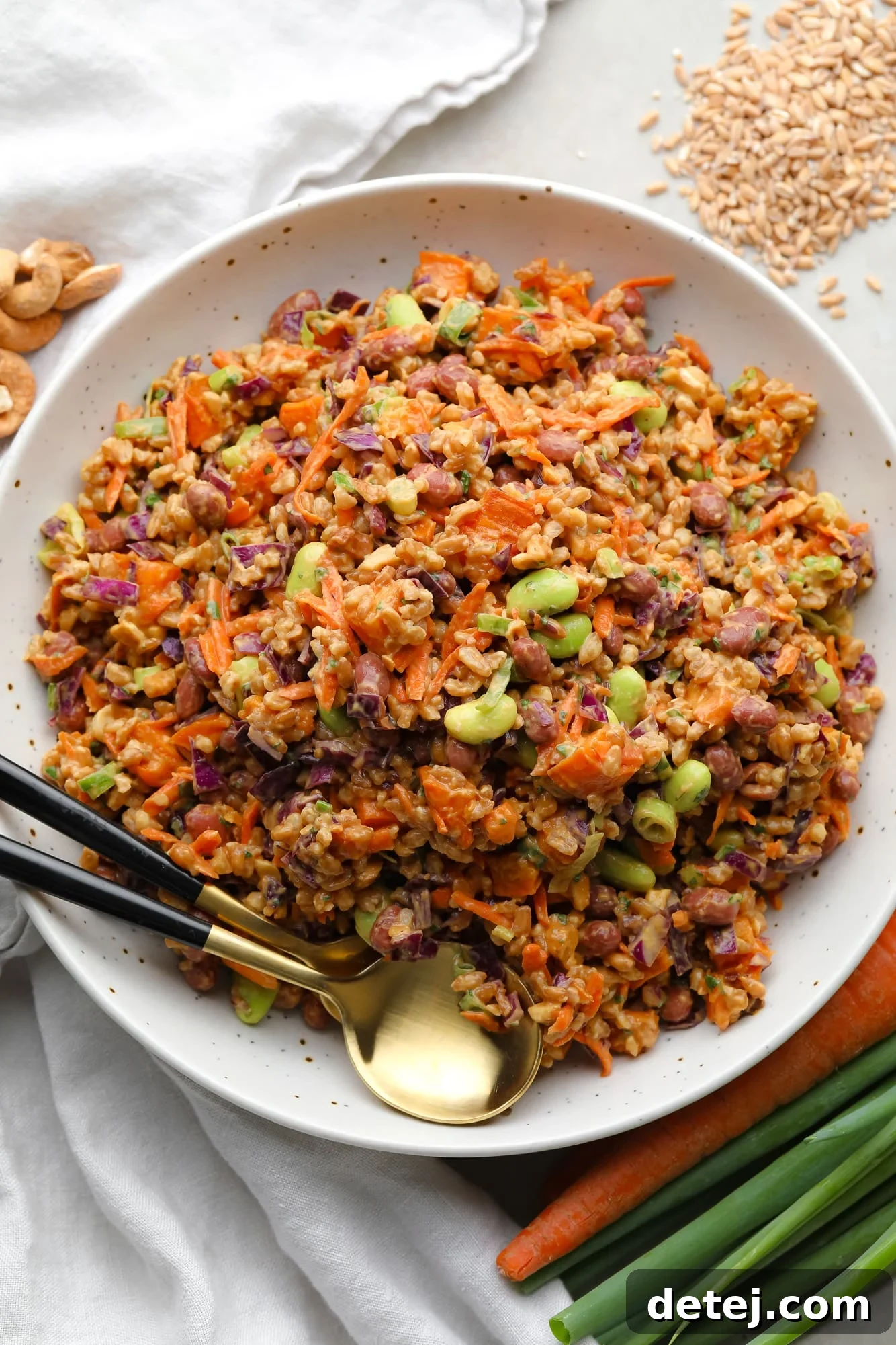 Spicy Peanut Farro Power Bowl 5 farro salad dressed in peanut sauce in a large white bowl with a gold spoon on the side.