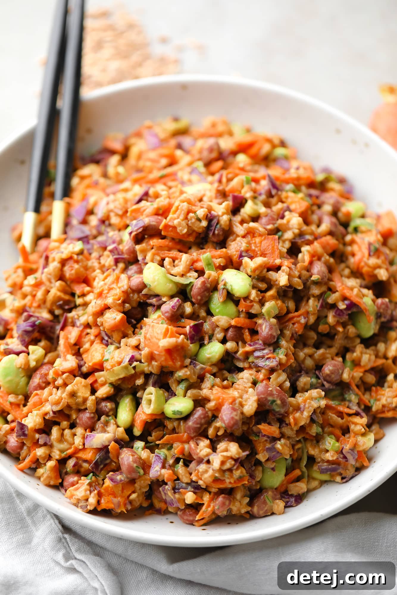 Spicy Peanut Farro Power Bowl 6 farro salad dressed in peanut sauce in a large white bowl with a gold spoon on the side.