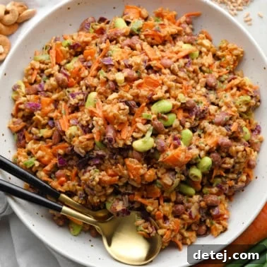 Spicy Peanut Farro Power Bowl 7 farro salad dressed in peanut sauce in a large white bowl with a gold spoon on the side.