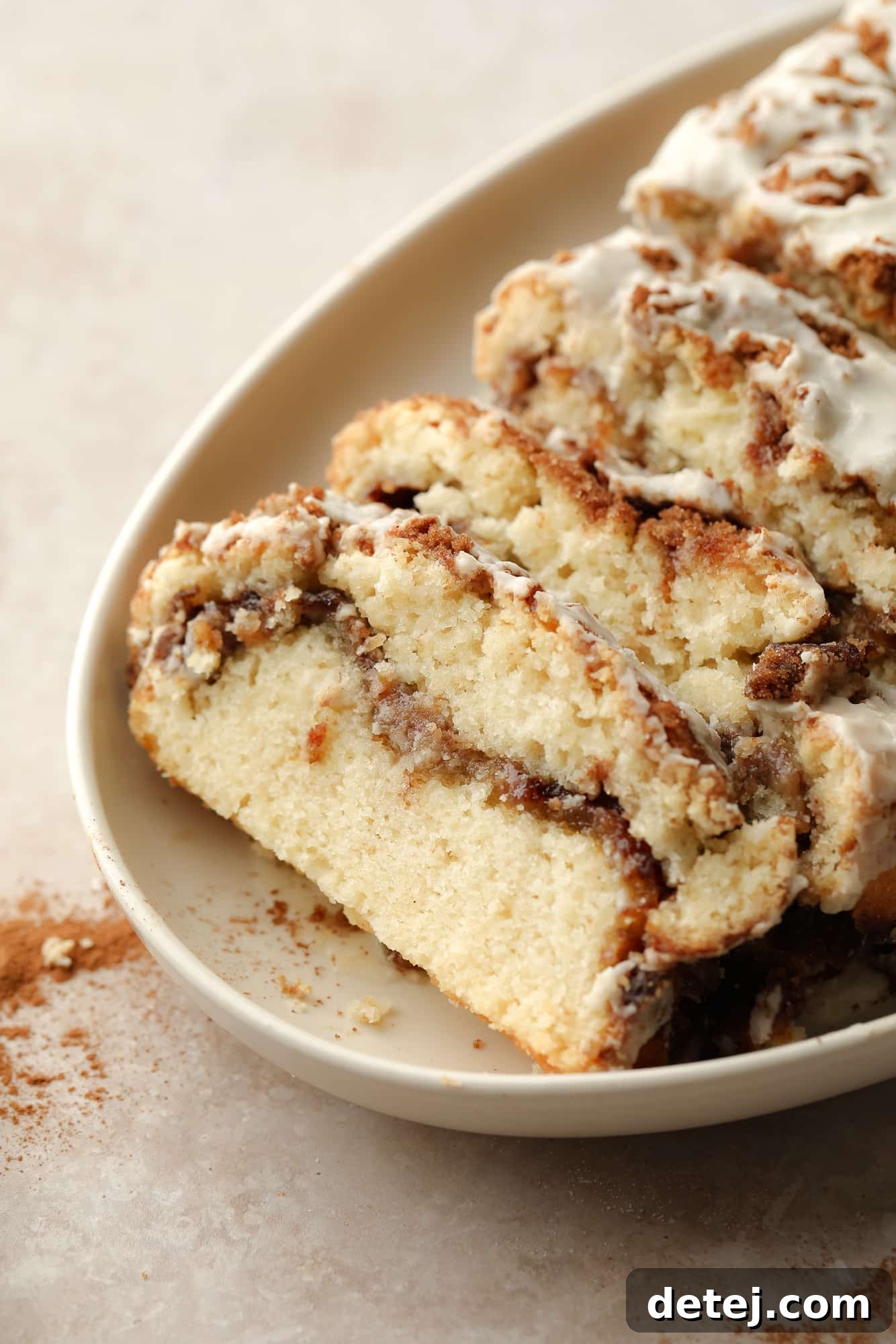 Slices of Vegan Cinnamon Swirl Quick Bread on a beige plate, showcasing the beautiful cinnamon swirl and vanilla glaze.