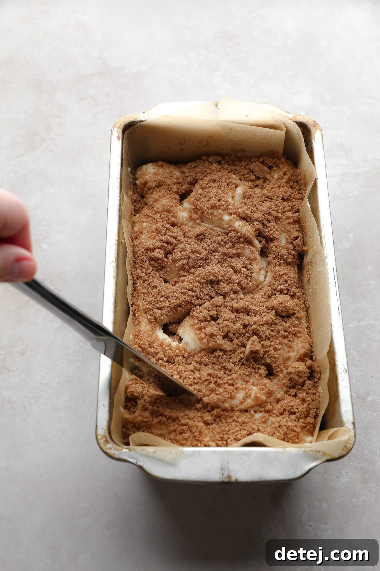 Using a knife to make a swirl pattern in bread batter, with cinnamon sugar on top, in a loaf pan.