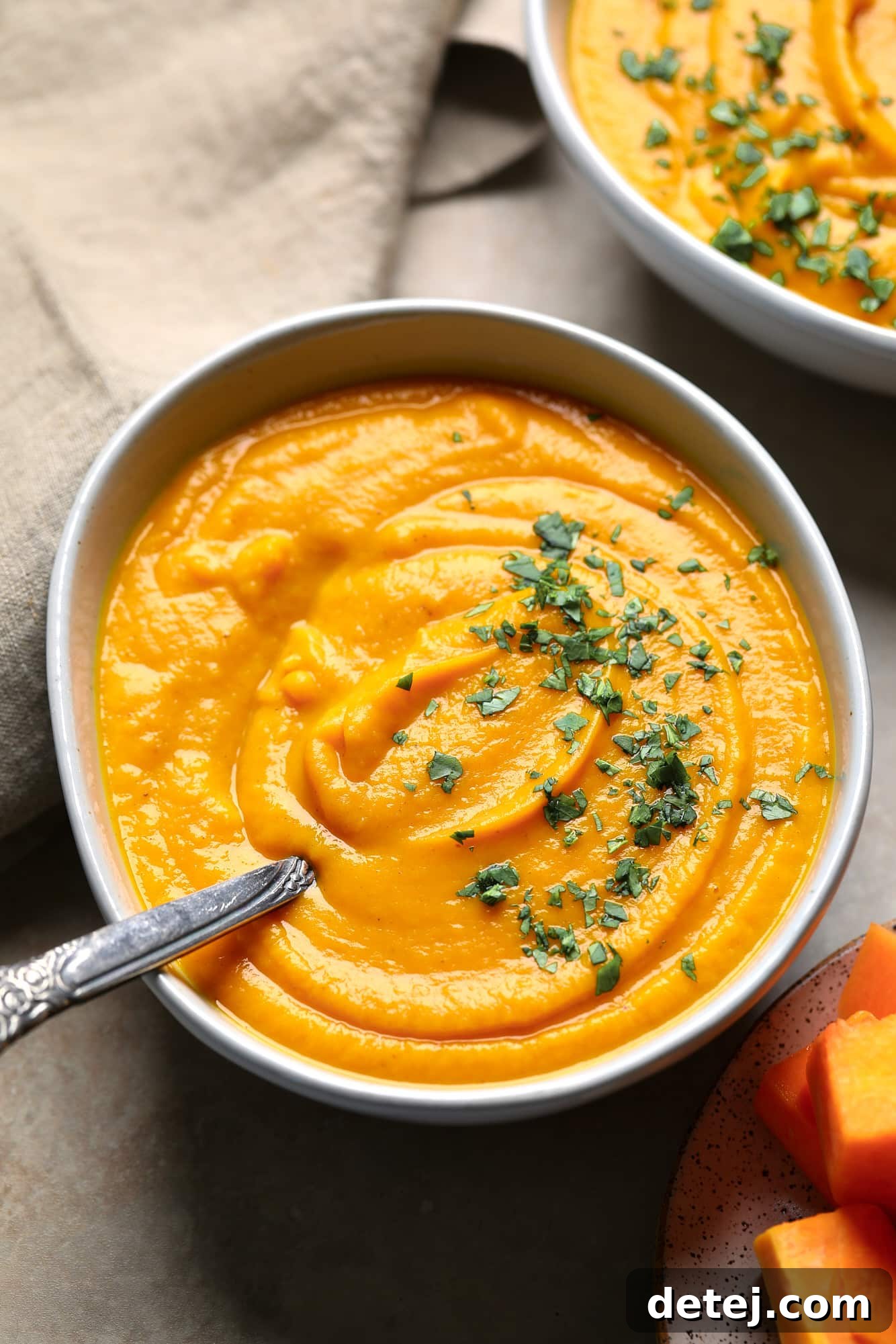 A beautifully presented bowl of creamy Butternut Squash and Sweet Potato Soup, garnished with fresh chopped herbs, evoking a cozy autumn feeling.