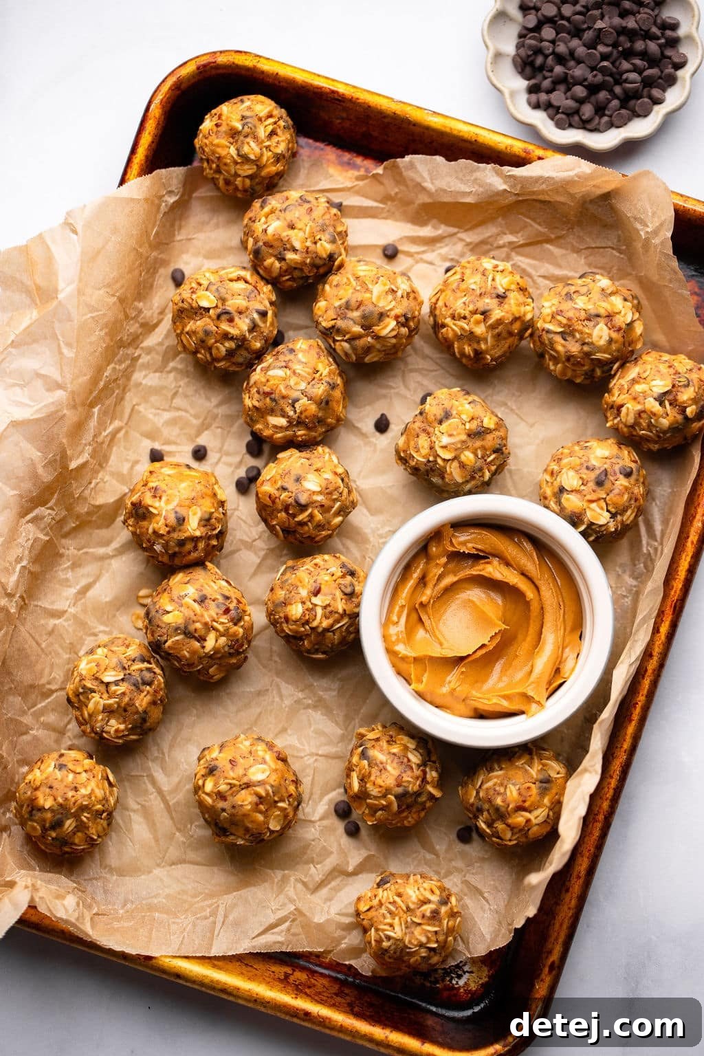 peanut butter energy balls next to a small bowl of peanut butter on a parchment lined baking sheet.