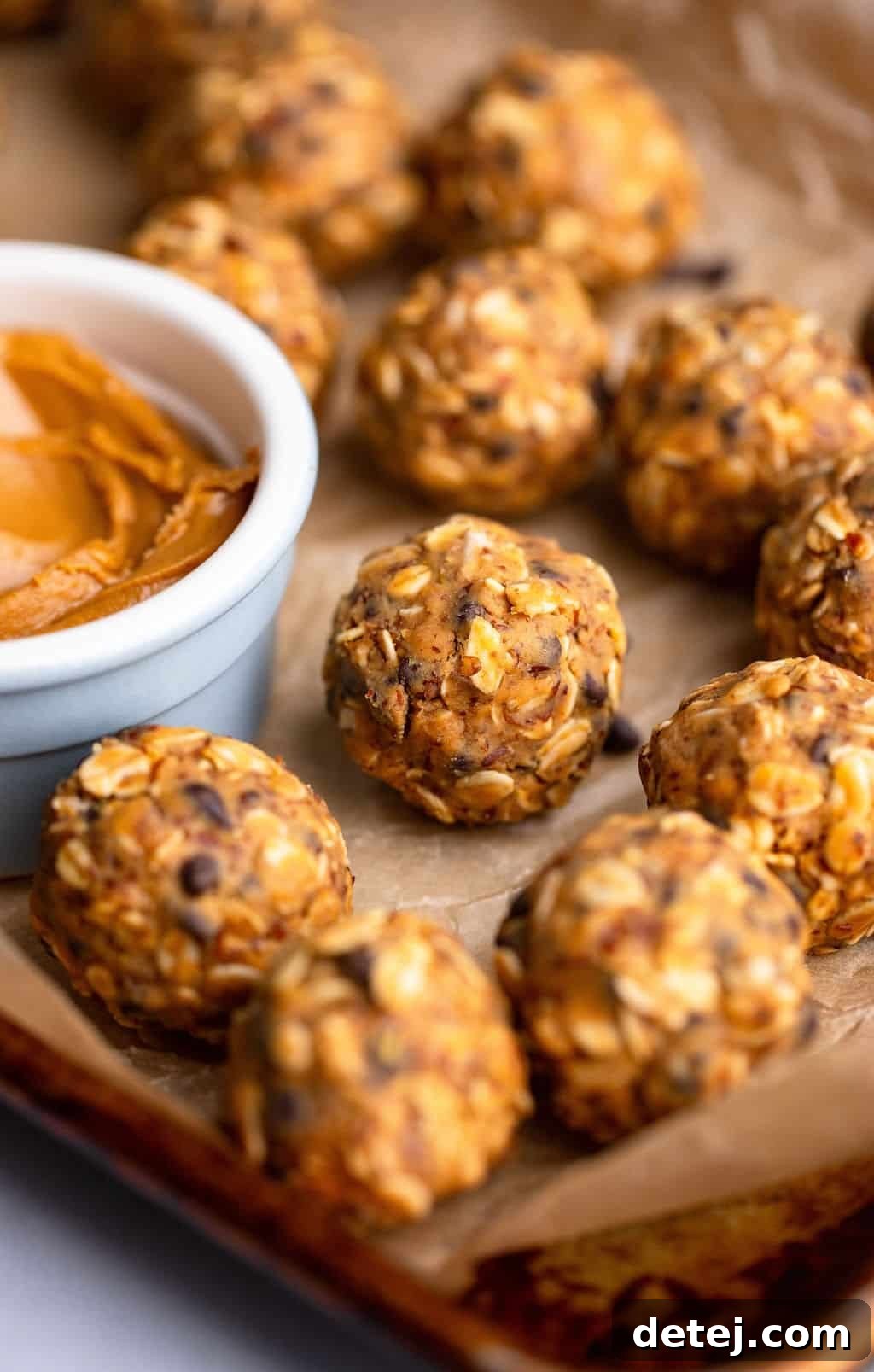 close up on peanut butter energy balls next to a small bowl of peanut butter on a parchment lined baking sheet.