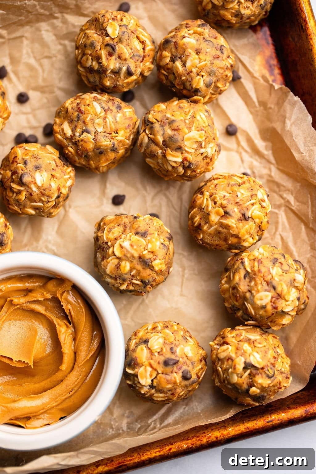 close up on peanut butter energy balls next to a small bowl of peanut butter on a parchment lined baking sheet.