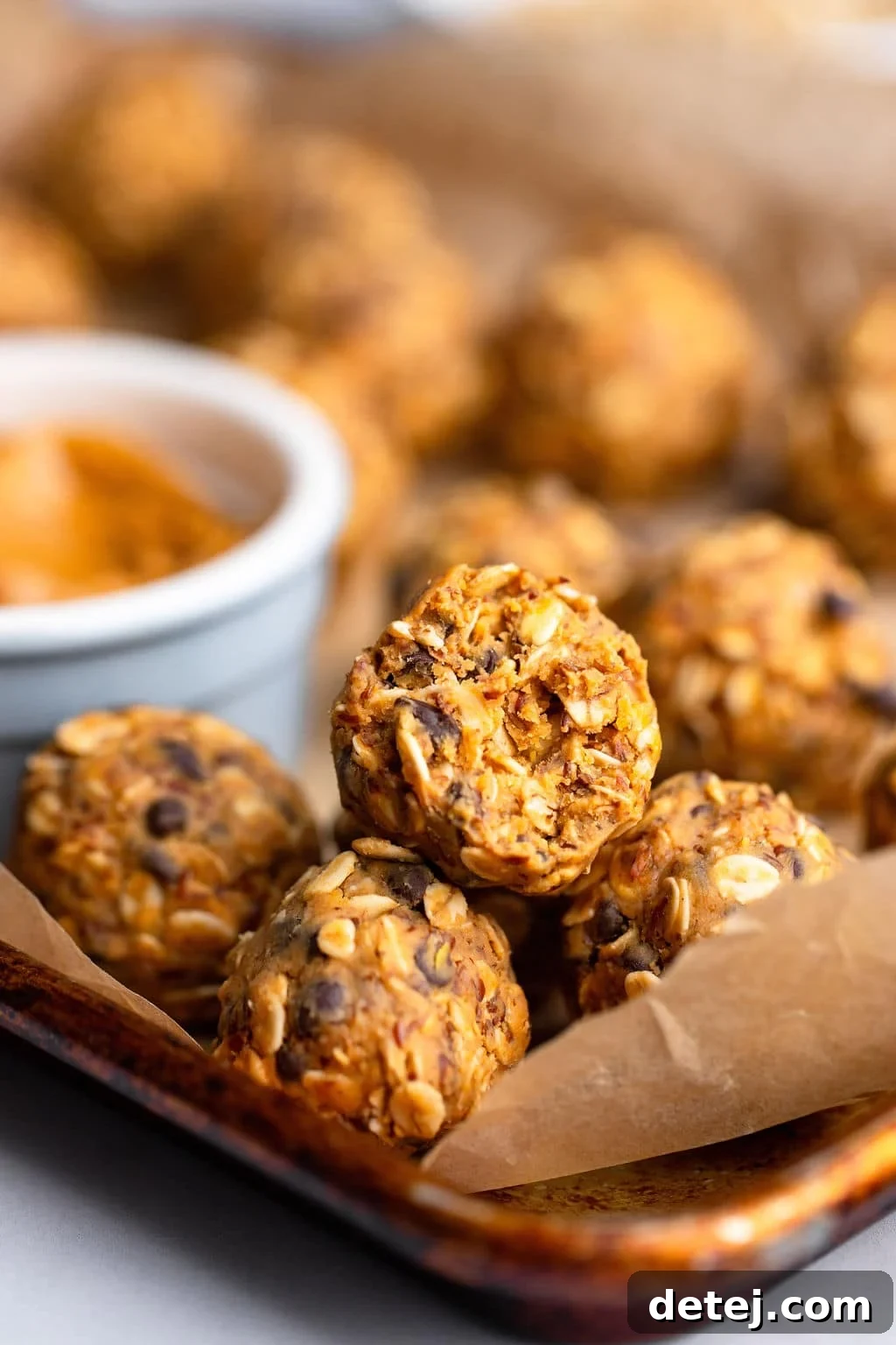 a peanut butter energy ball with a bite taken out of it on a parchment-lined baking sheet.