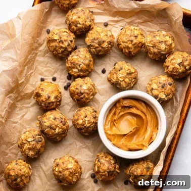 close up on peanut butter energy balls next to a small bowl of peanut butter on a parchment lined baking sheet.
