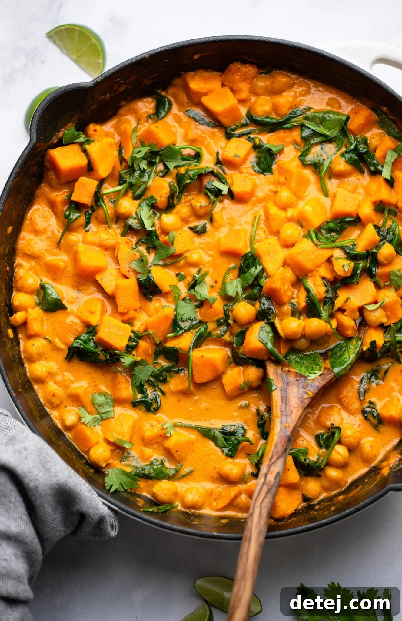 using a wooden spoon to scoop sweet potato curry in a black skillet.