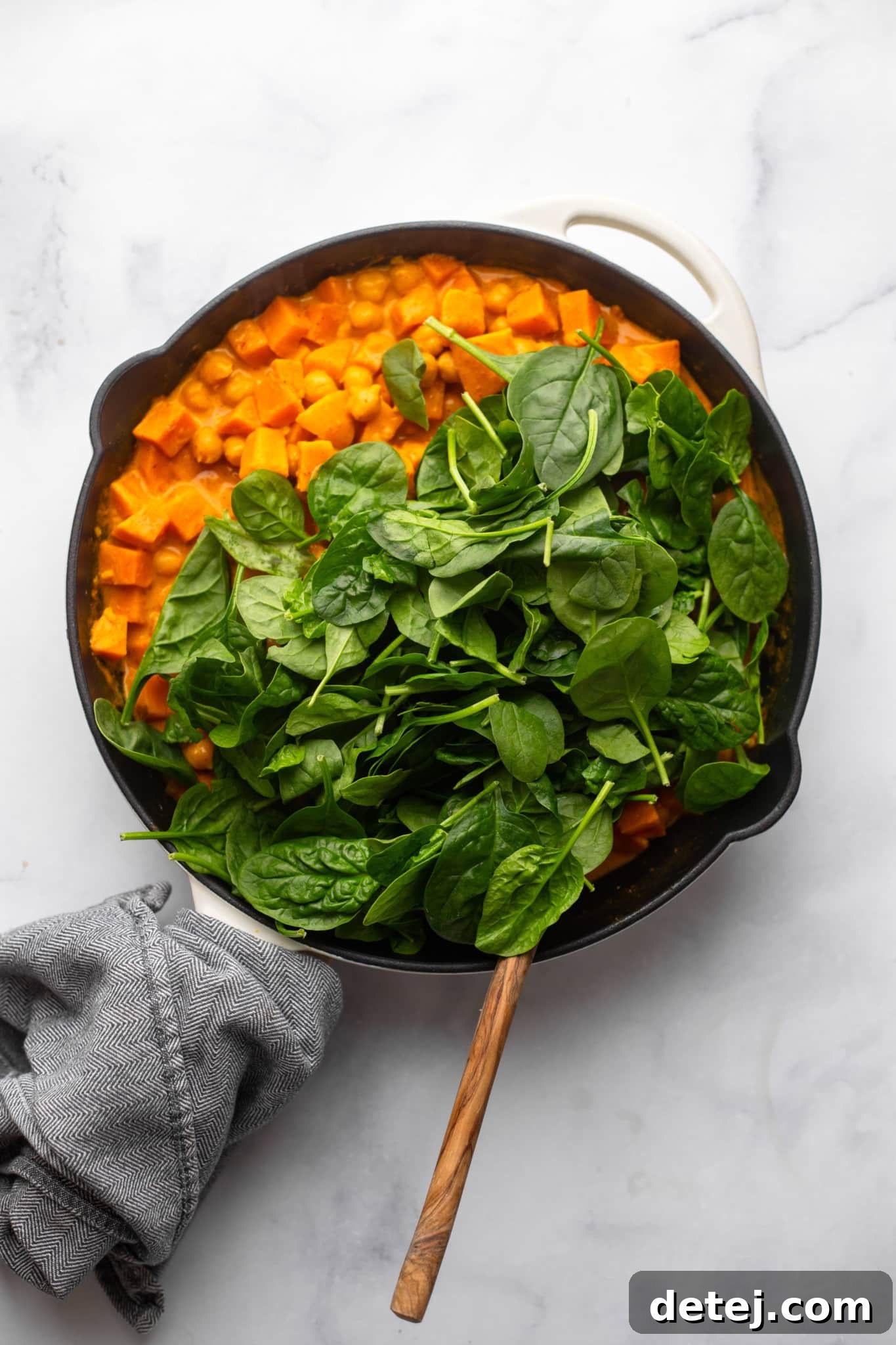 fresh spinach on top of red curry in a black skillet.