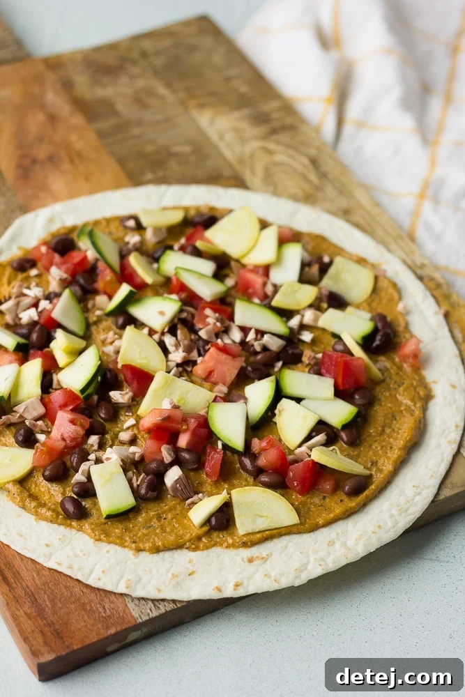 Hands adding black beans and chopped vegetables to a tortilla spread with vegan cheese for quesadillas