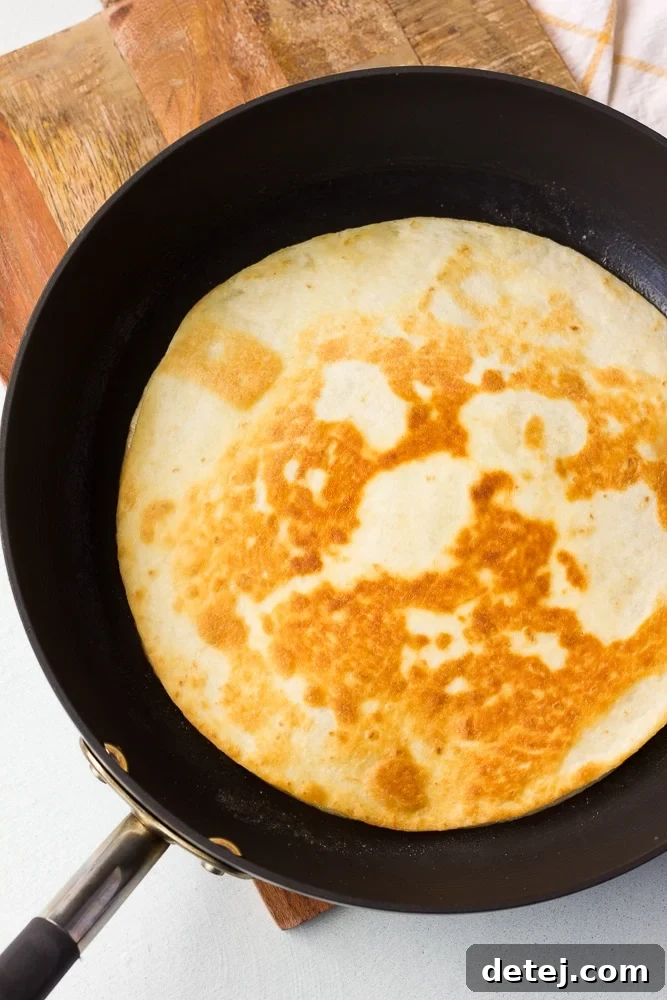A vegan quesadilla cooking on a hot pan, showing a golden brown tortilla