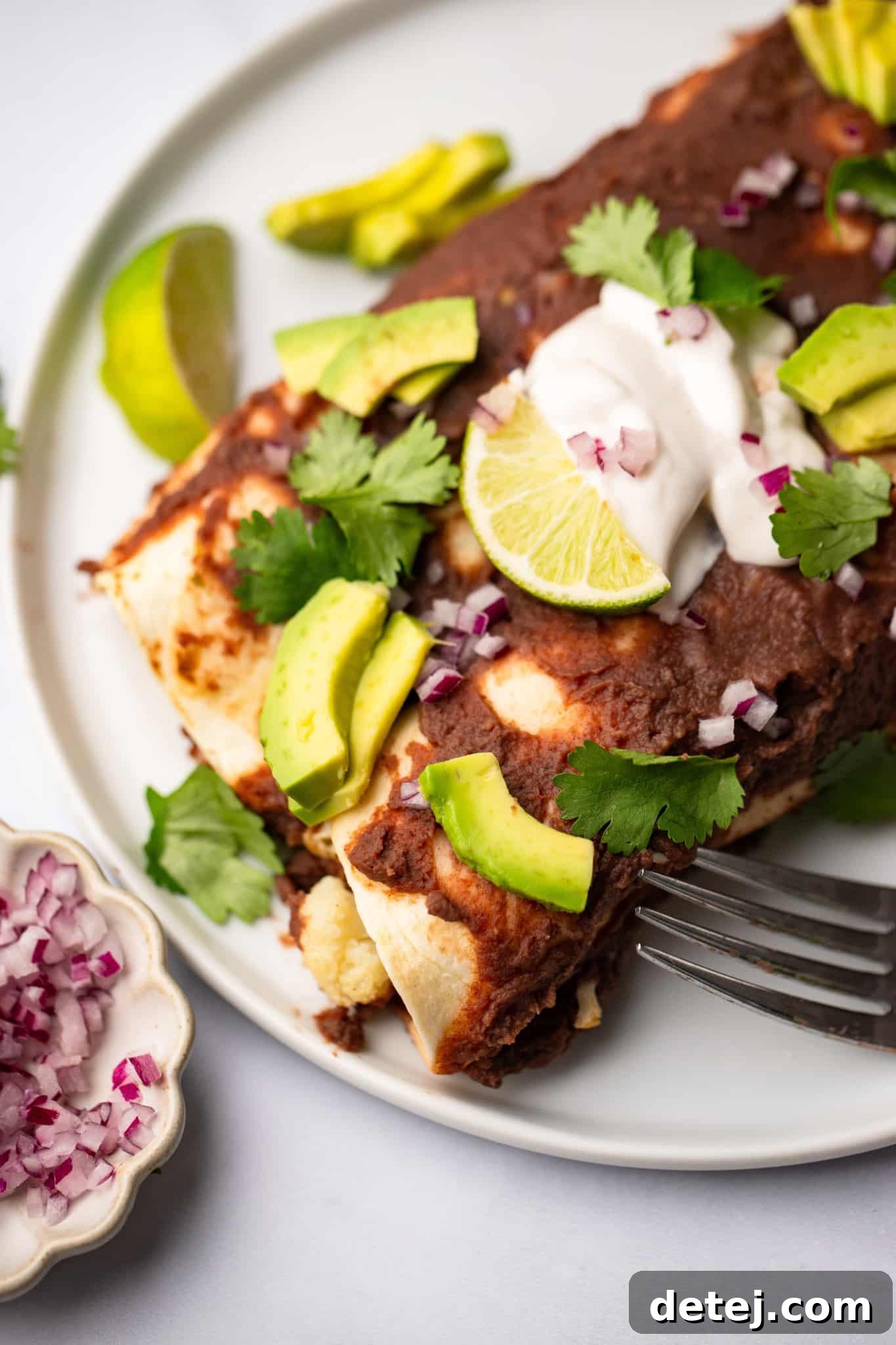 Close up on Roasted Veggie Enchiladas with Black Bean Sauce on a white plate with a fork on the side, highlighting the rich flavors and vibrant textures.