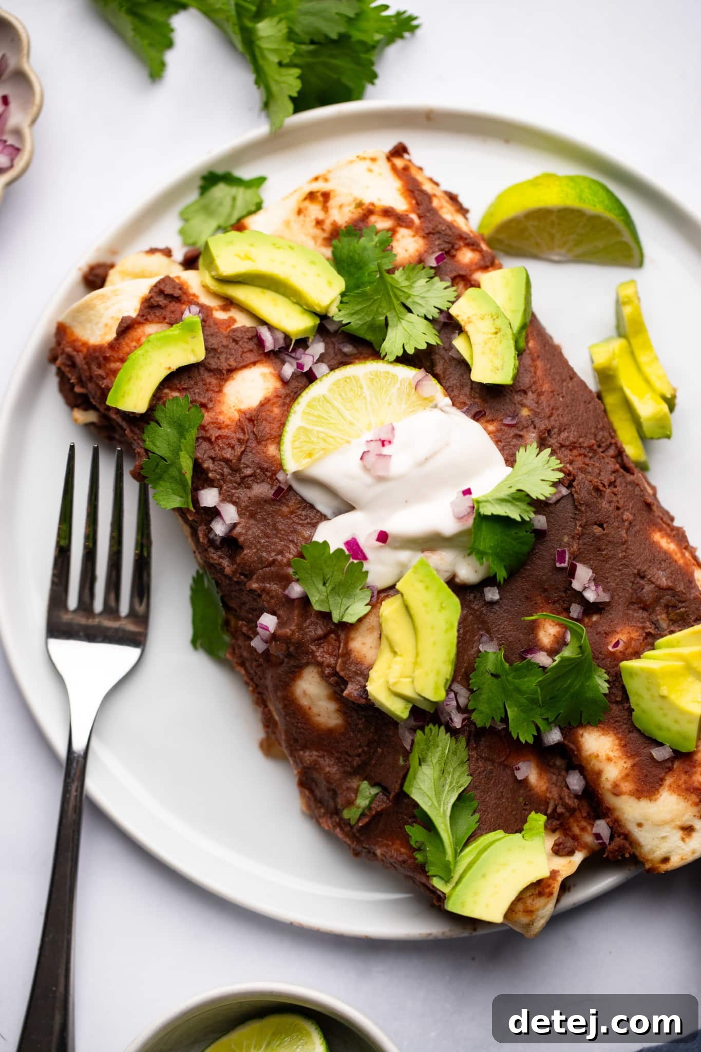 Two perfectly portioned Roasted Veggie Enchiladas with Black Bean Sauce on a white plate, served with a fork, ready to be enjoyed.