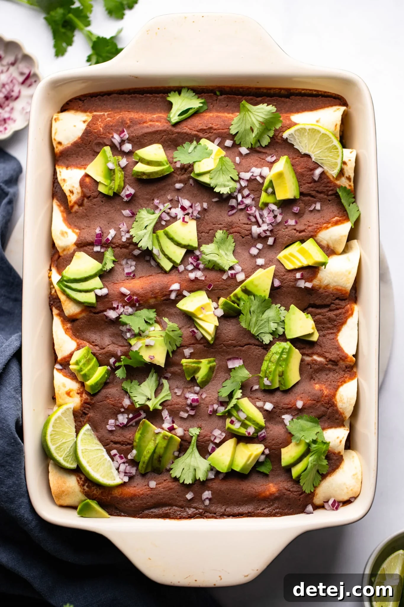 Roasted Veggie Enchiladas with Black Bean Sauce topped with fresh avocado, red onions, and cilantro in a vibrant baking dish, showcasing a wholesome meal.