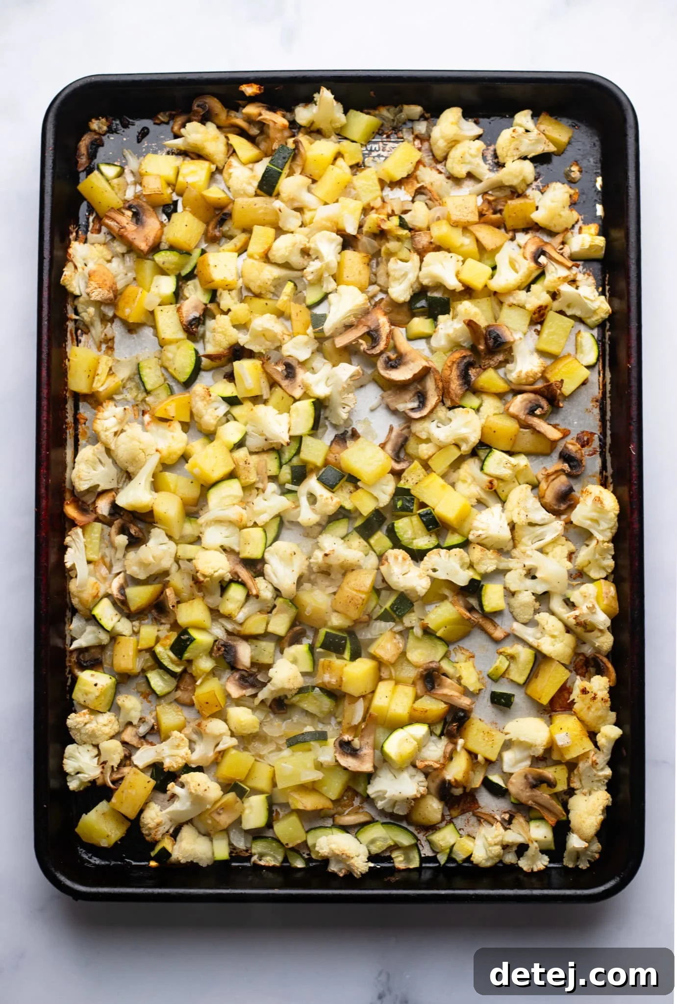 Vibrant assortment of seasoned, chopped vegetables ready for roasting on a baking sheet, featuring potatoes, zucchini, and cauliflower.