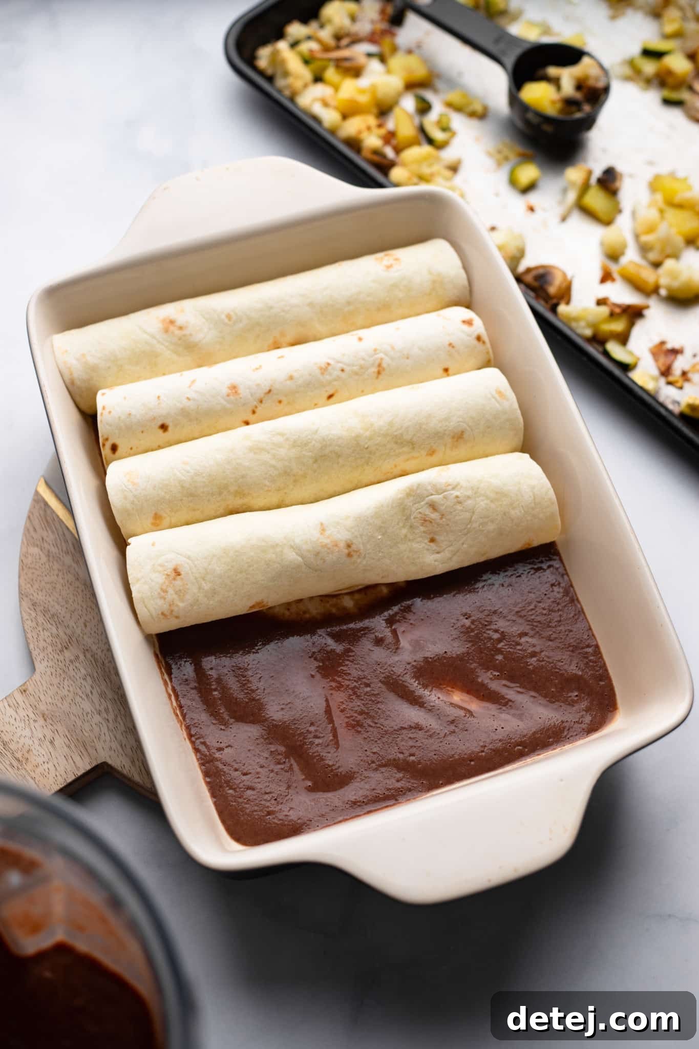 Hands carefully assembling Roasted Veggie Enchiladas with Black Bean Sauce in a baking dish, showcasing the filling process.