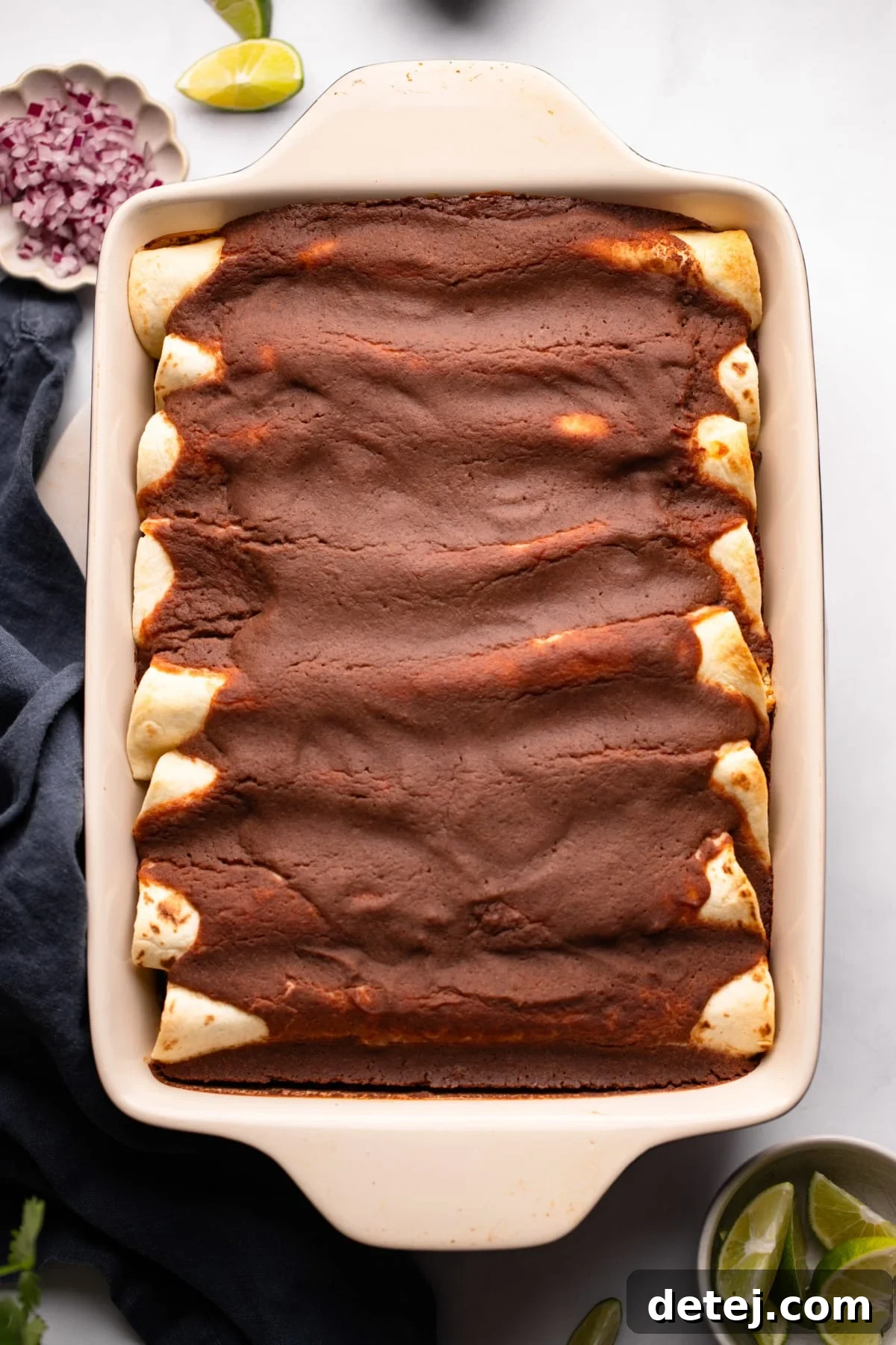 Glorious baked veggie enchiladas covered in a rich black bean sauce, bubbling hot in a baking dish, fresh out of the oven.