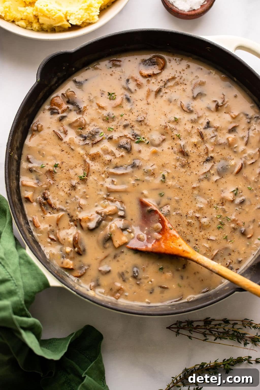 stirring mushroom gravy in a black skillet with a wooden spoon.