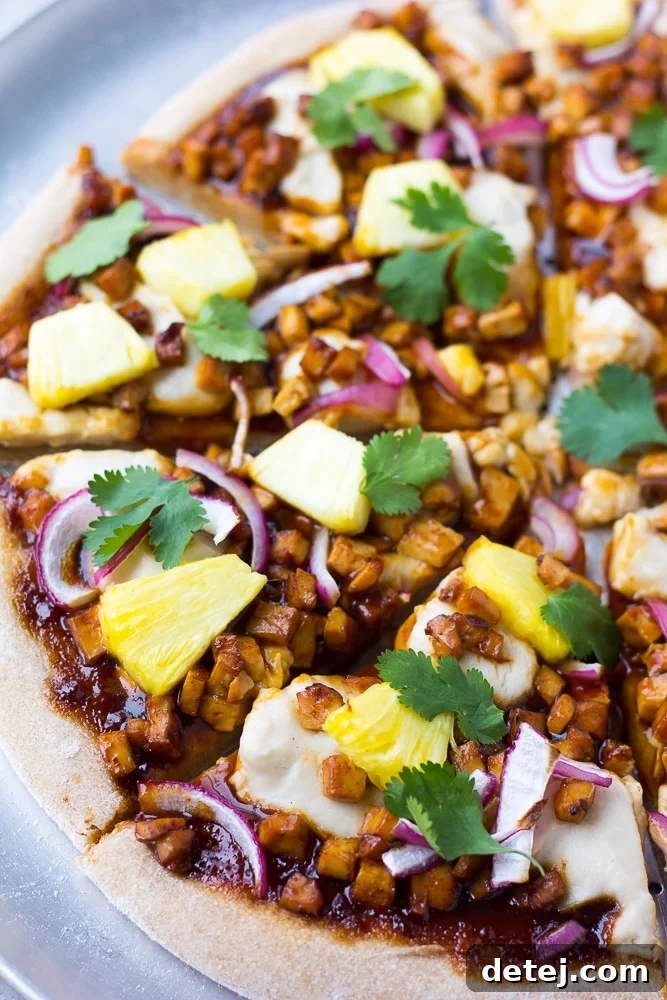 Close-up shot of a baked Hawaiian BBQ Vegan Pizza slice, showing melted vegan cheese, barbecue tofu, pineapple, and red onion.