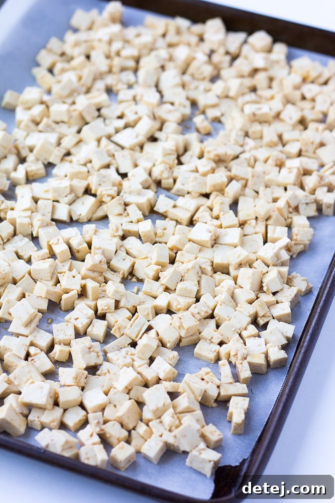 Unbaked tofu pieces, seasoned with soy sauce, neatly arranged on a parchment-lined baking sheet before oven baking.