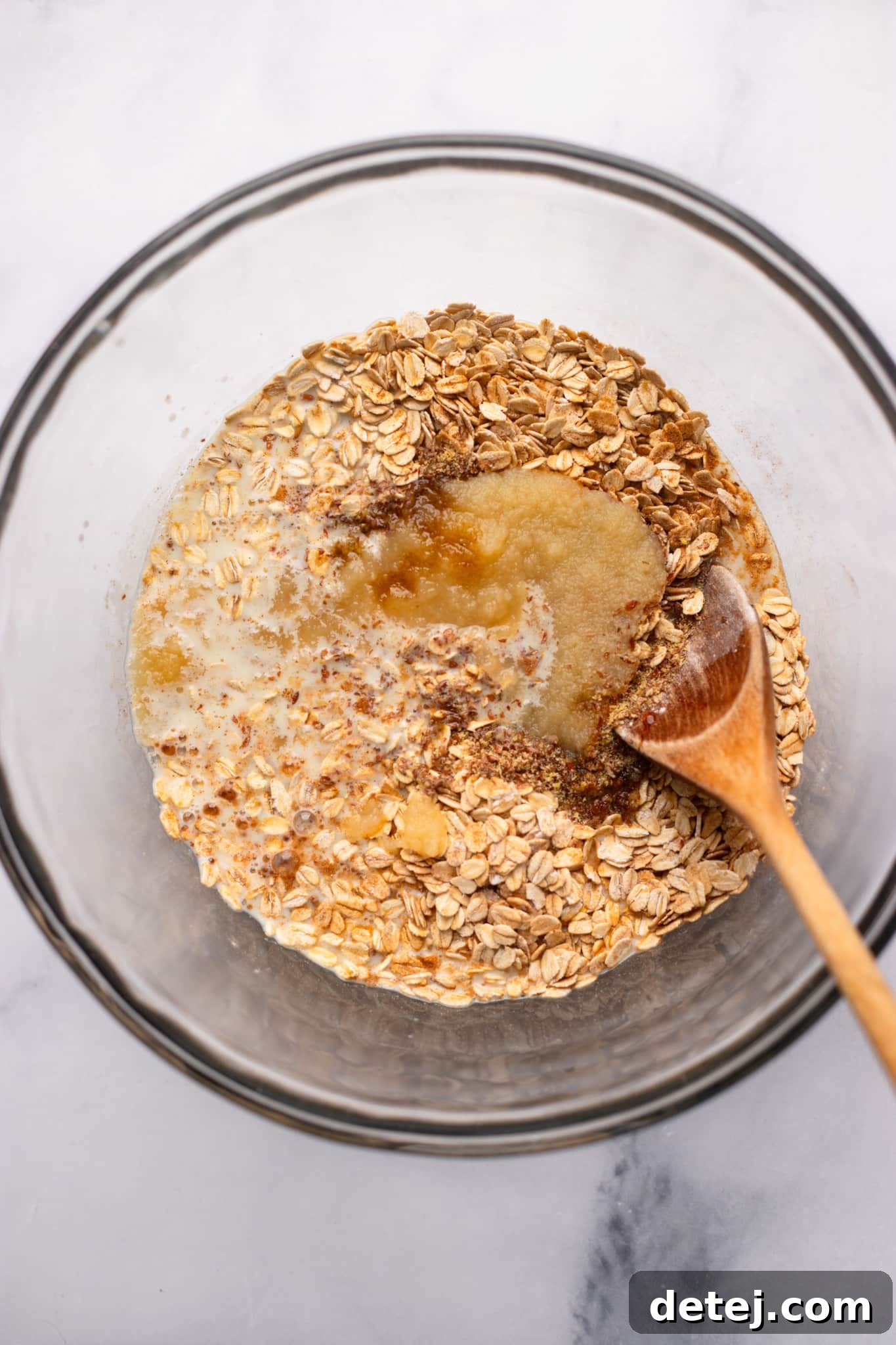 Warm Apple Oat Bake 5 A wooden spoon mixing wet and dry ingredients in a glass bowl to create the oatmeal base for baked apple oatmeal.