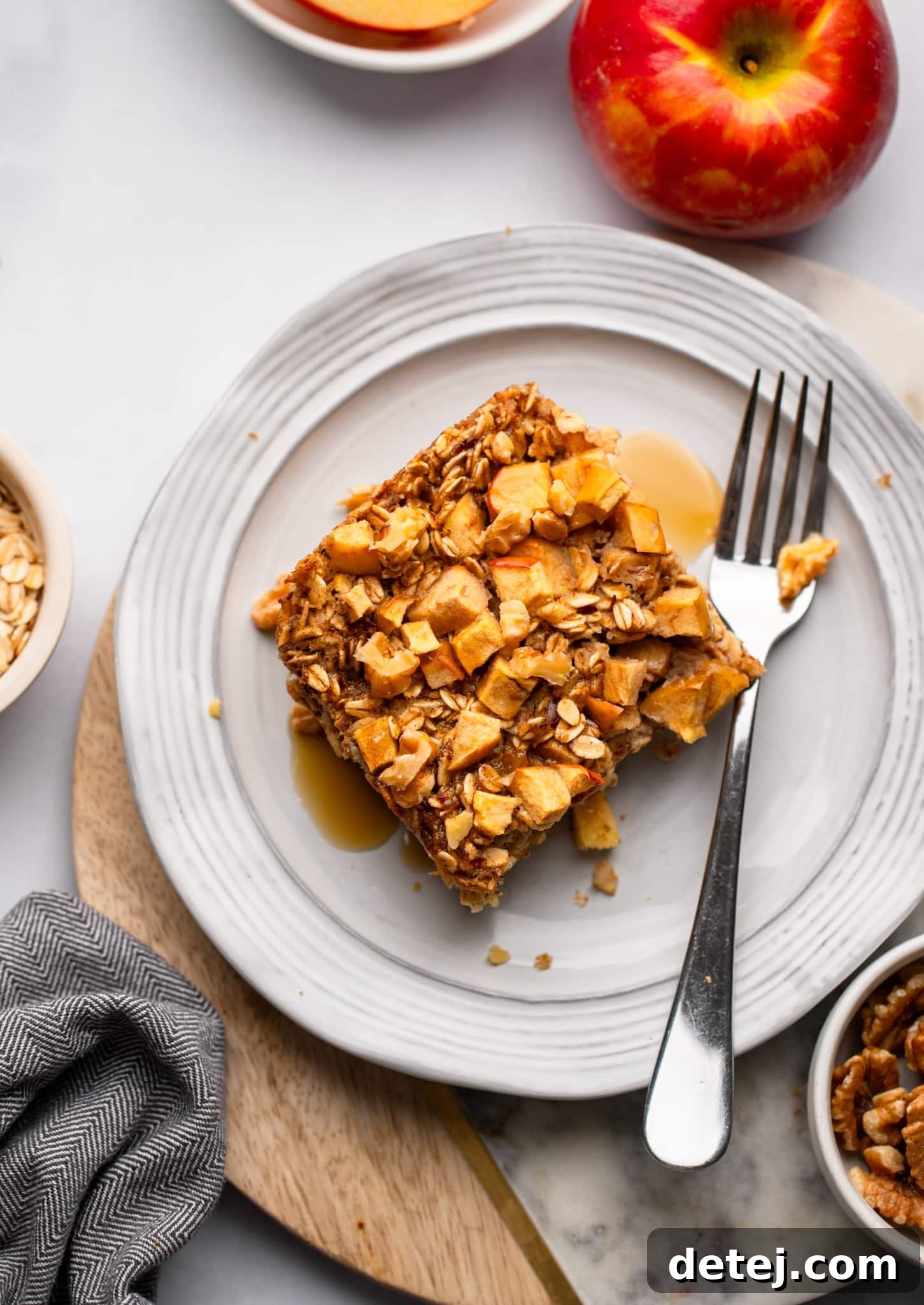 Warm Apple Oat Bake 8 A single slice of Apple Baked Oatmeal on a white plate, with a fork beside it, showcasing its texture.