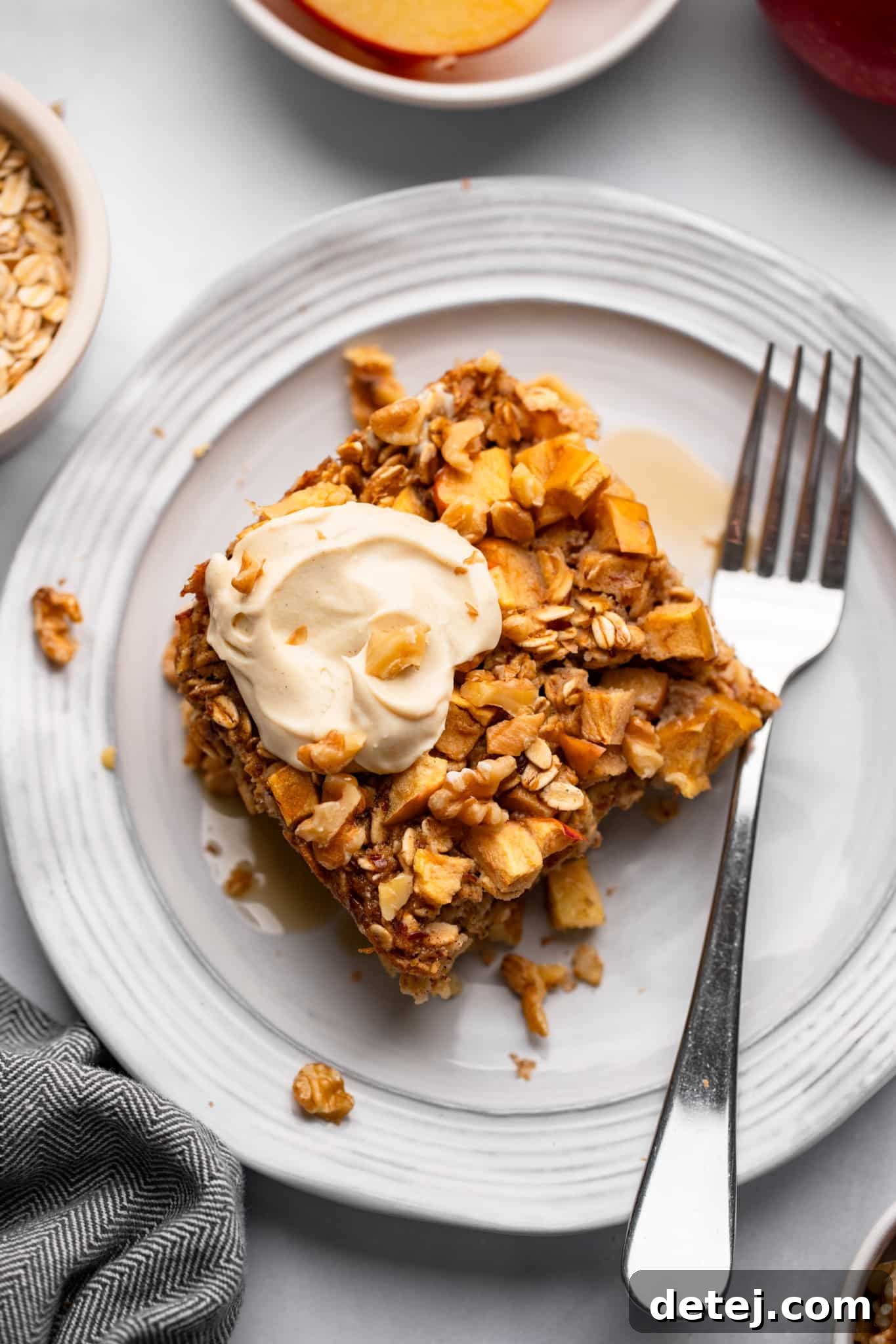 Warm Apple Oat Bake 9 A delicious slice of Apple Baked Oatmeal topped with a dollop of creamy vegan yogurt, presented on a white plate with a fork.