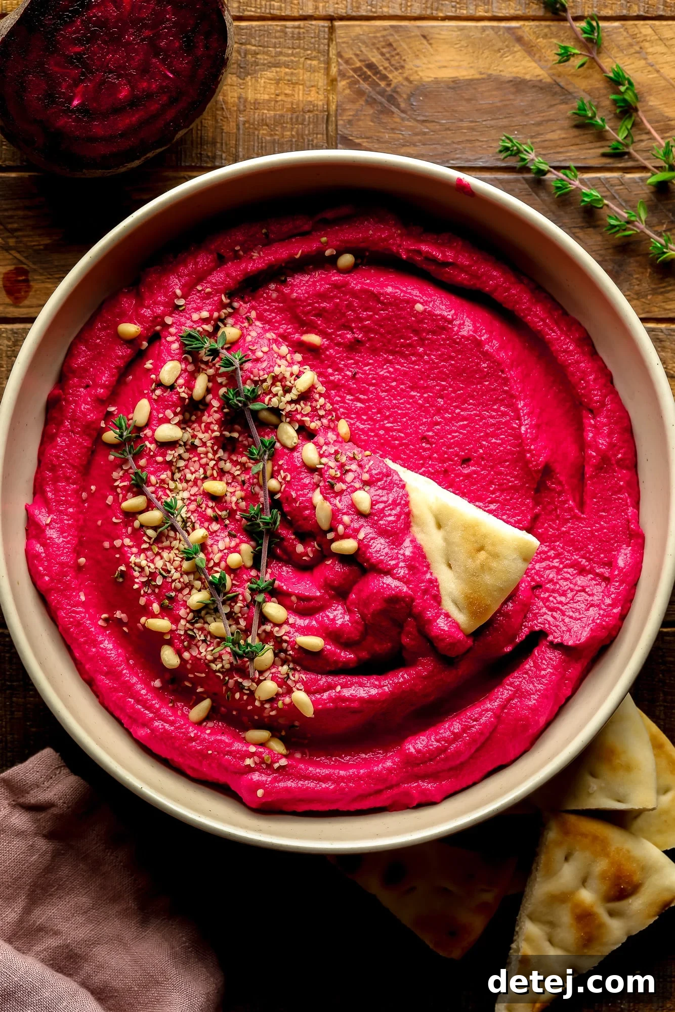 Ruby Red Hummus 2 A bowl of vibrant pink beet hummus, elegantly garnished with pine nuts and fresh thyme sprigs, ready to be enjoyed.