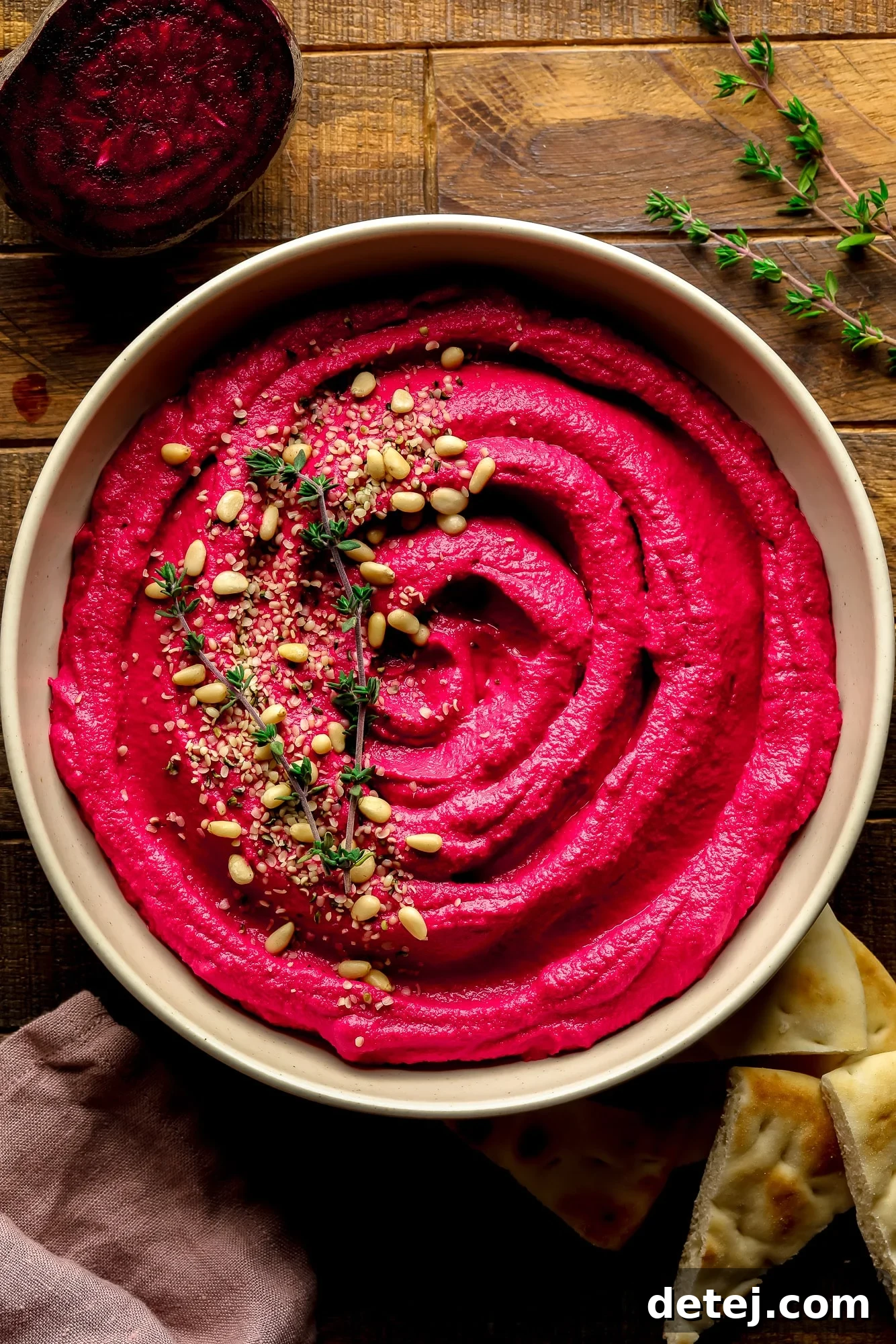 Ruby Red Hummus 6 A beautifully presented bowl of pink beet hummus, garnished with toasted pine nuts and fresh thyme, showcasing its vibrant color and inviting texture.
