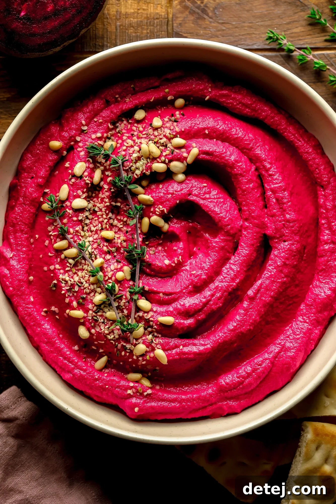 Ruby Red Hummus 7 A close-up of a bowl of vibrant pink beet hummus, adorned with pine nuts and fresh thyme, highlighting its creamy texture.