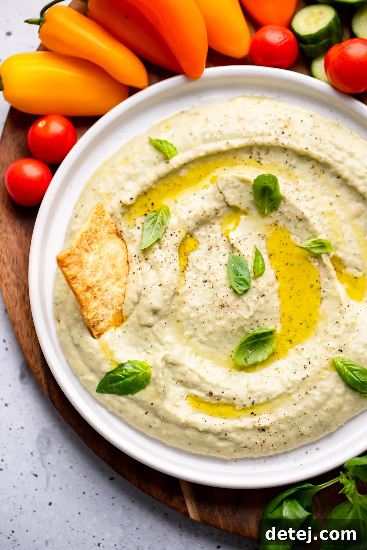 close up on white bean dip in a white bowl surrounded by vegetables and crackers.