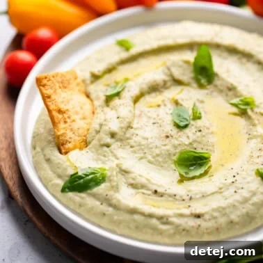 close up on white bean dip in a white bowl with a cracker pushed in the dip.