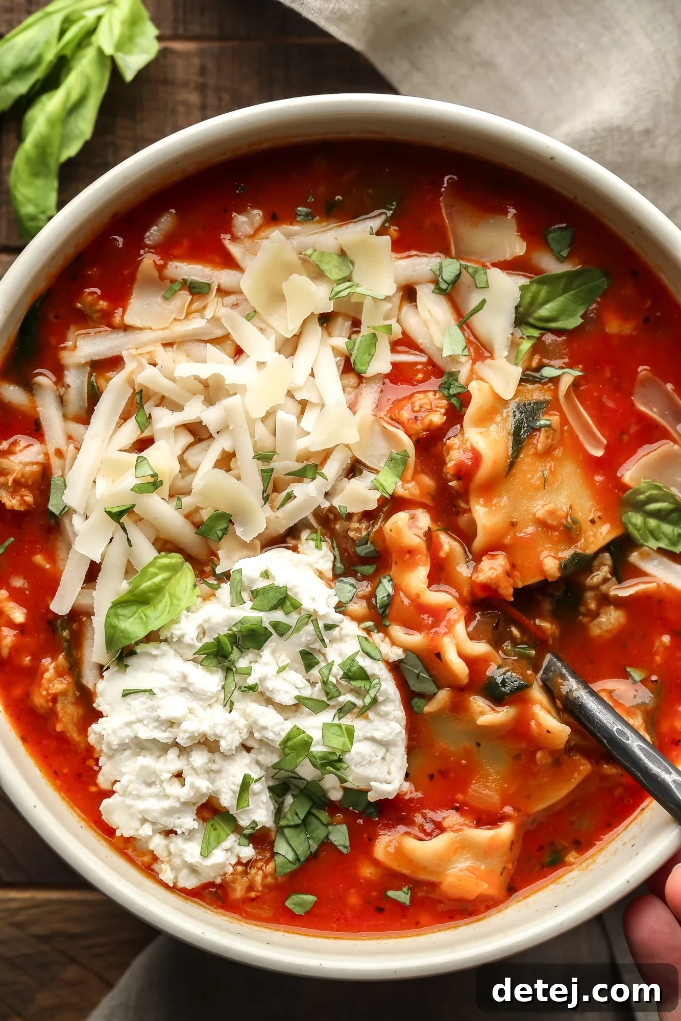 close up on a bowl of vegan lasagna soup topped with chopped basil, vegan mozzarella, and vegan ricotta cheese.