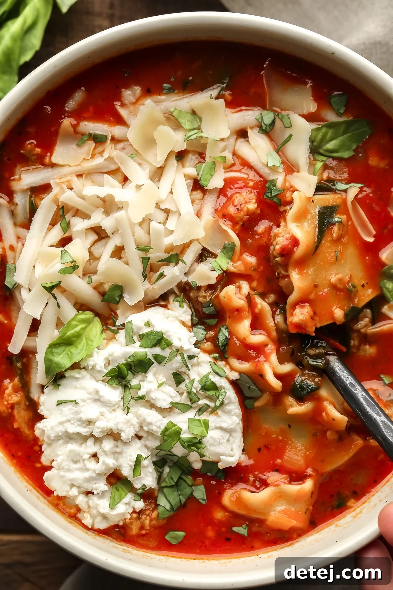close up on a bowl of vegan lasagna soup topped with chopped basil, vegan mozzarella, and vegan ricotta cheese.