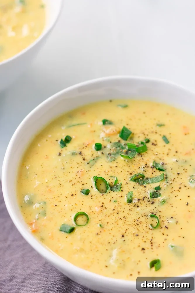 A close-up view of creamy vegan cauliflower soup in a white ceramic bowl, garnished with a sprig of fresh dill.