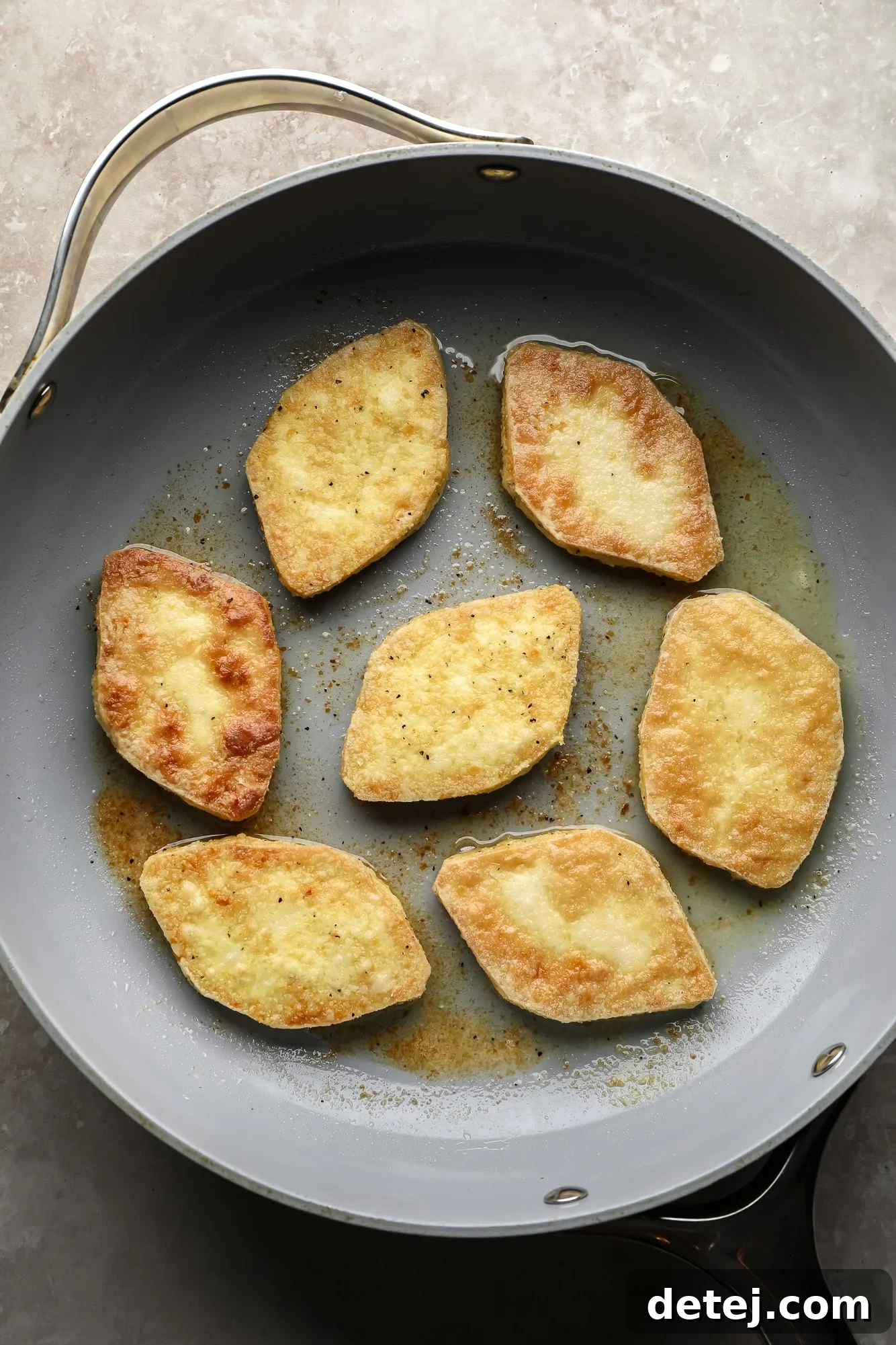 Close-up of tofu pieces frying in a large skillet, developing a golden and crispy exterior.