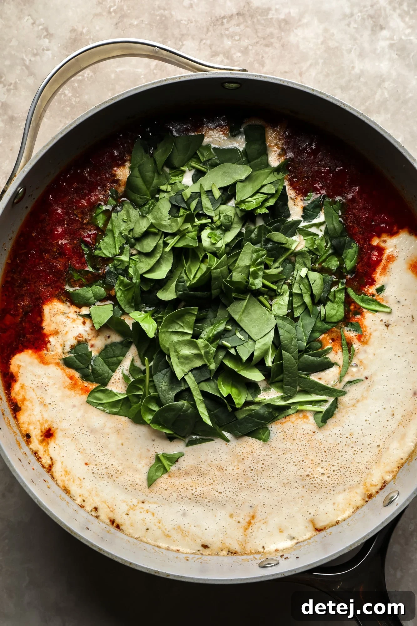 Adding fresh baby spinach to the simmering creamy sun-dried tomato sauce in a large skillet for Marry Me Tofu.